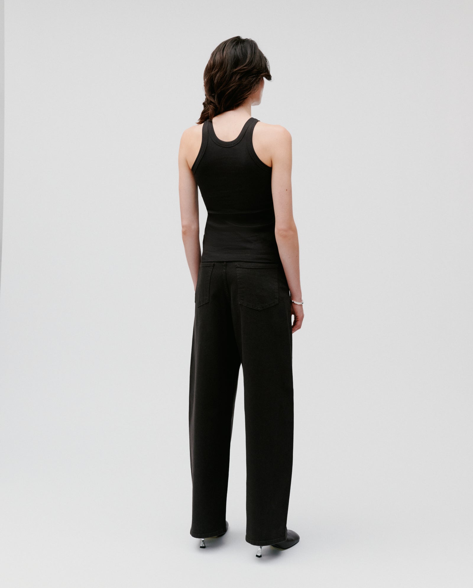 A person stands with their back to the camera, wearing the black FINLEY Top by IVY OAK and black pants against a plain background.