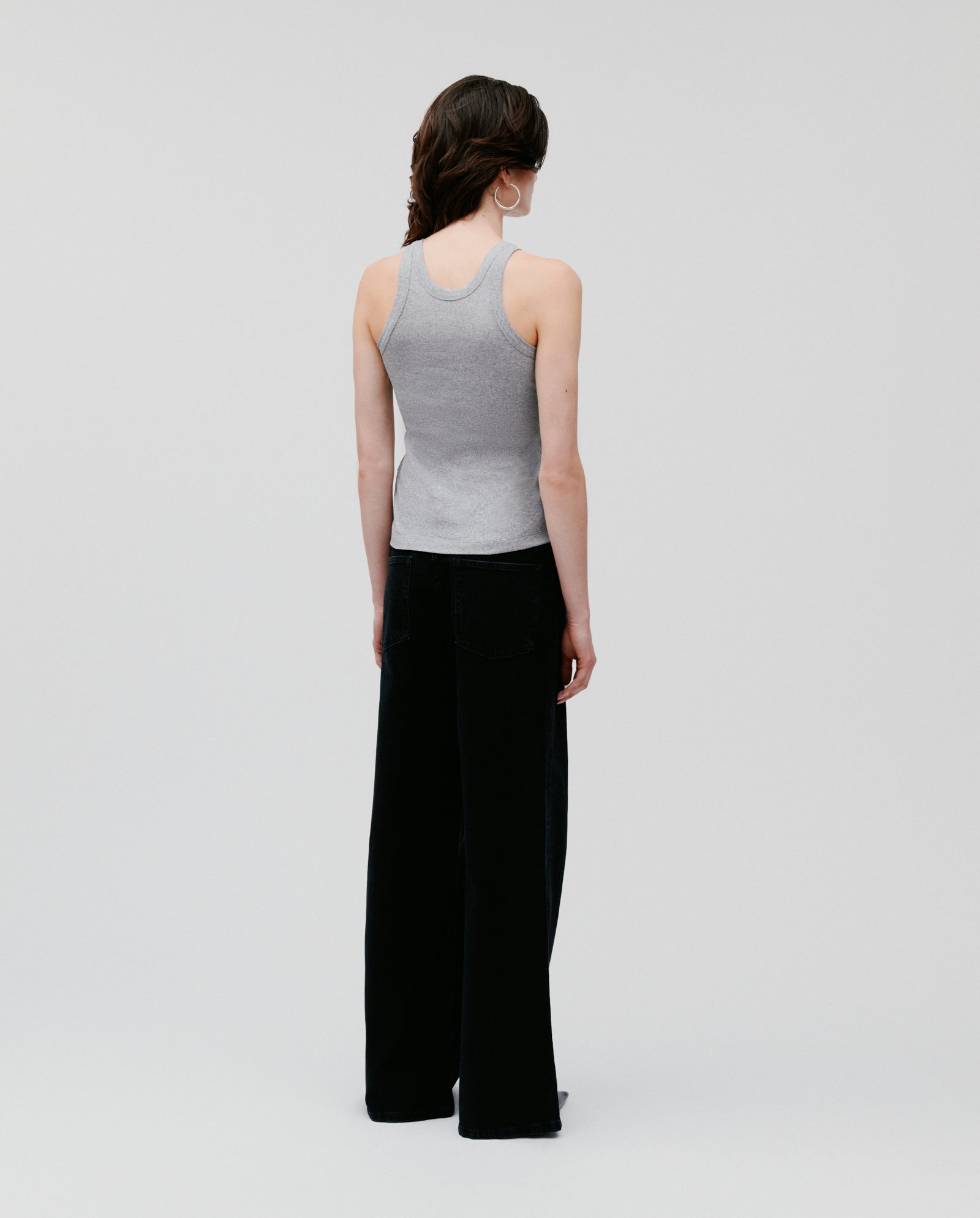 A woman faces away, wearing the IVY OAK FINLEY Top—a womens sleeveless ribbed tank—paired with black wide-leg pants, set against a plain background.