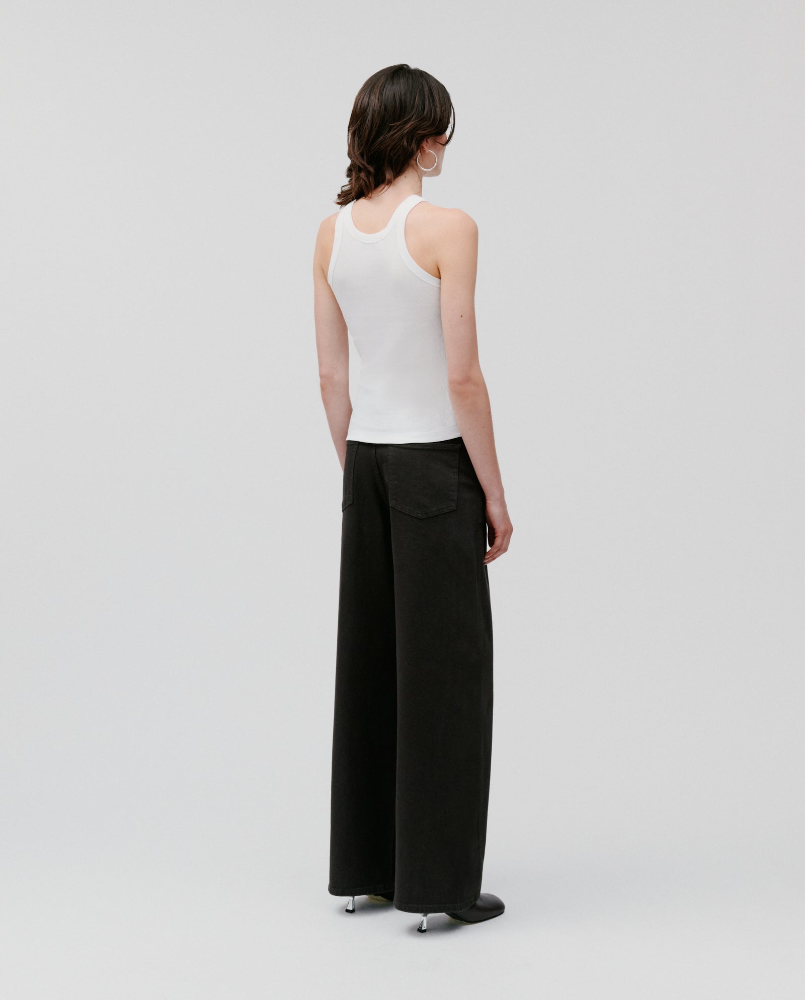 A person wearing the IVY OAK FINLEY Top, a womens sleeveless ribbed tank, paired with black wide-leg pants, stands facing away against a plain background.