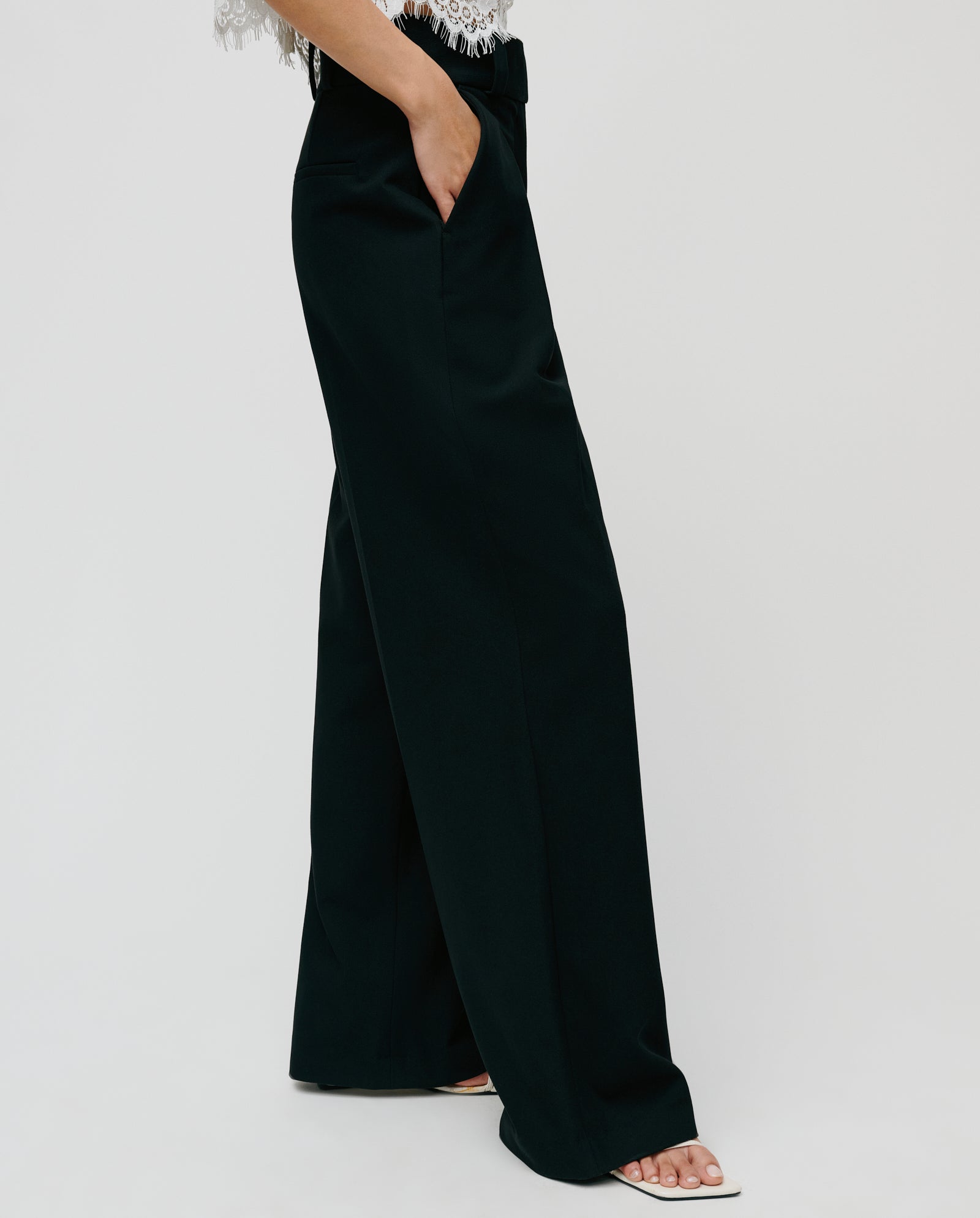 Model wearing IVY OAKs PEONY ROSE Trouser, styled high-waisted with a lace top and open-toe heels, hand in pocket, set against a plain background.