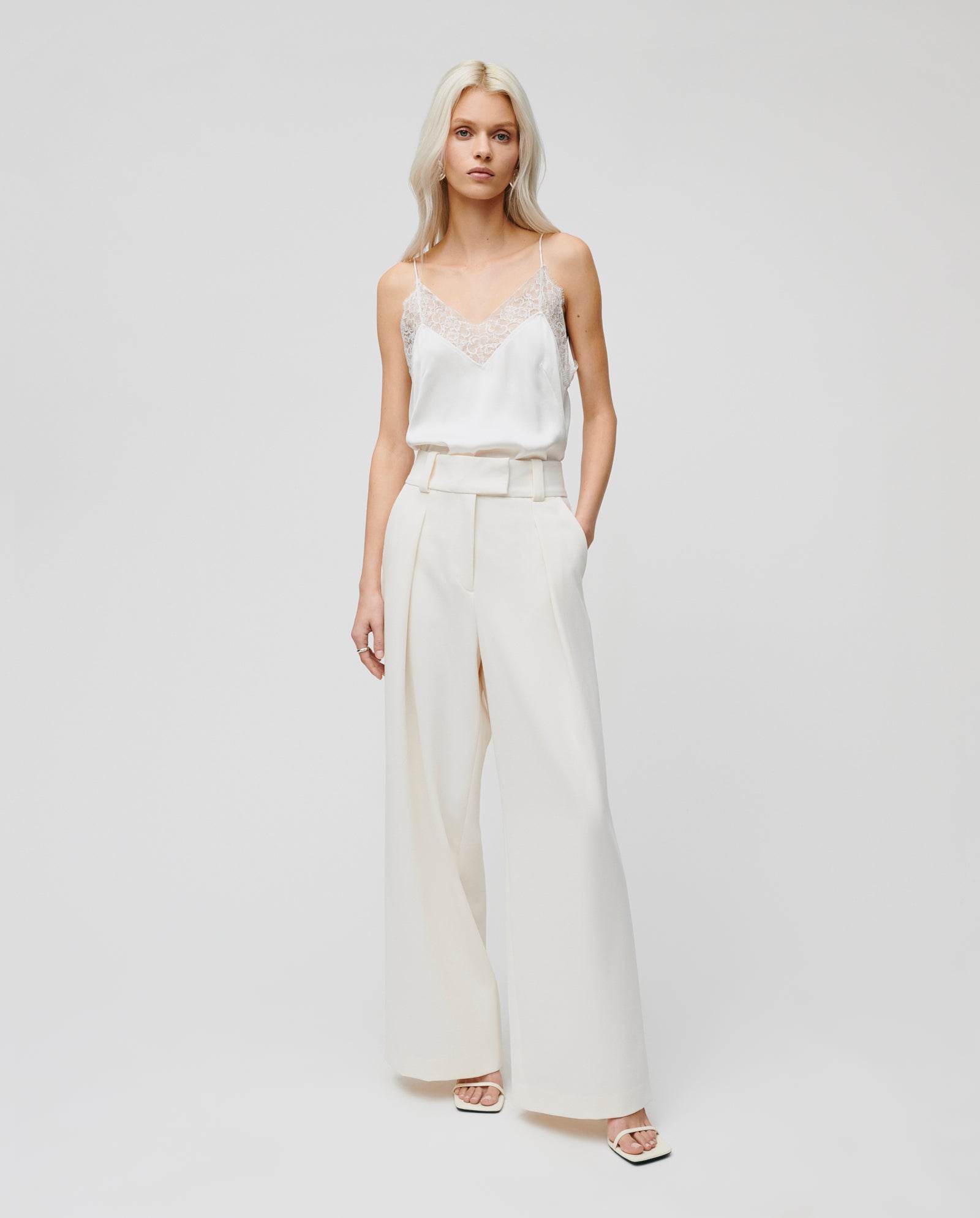 A woman stands against a plain background wearing IVY OAKs PEONY ROSE Trouser, a high-waist viscose-blend wide-leg pant, paired with a white lace-trim camisole.