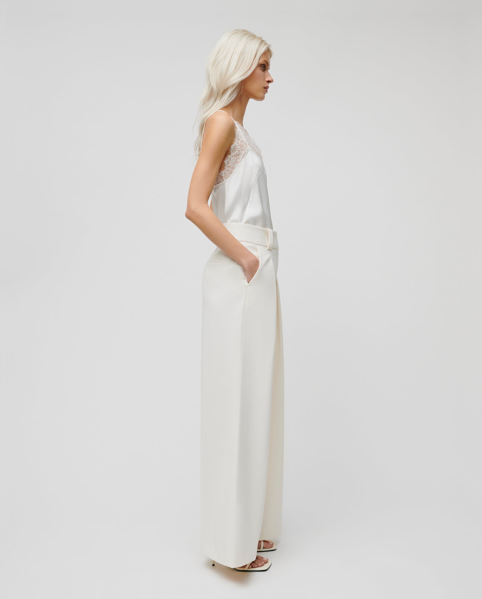 Woman wearing IVY OAKs PEONY ROSE Trouser, a high-waisted wide leg pant, paired with a silky sleeveless lace top, standing in profile against a plain background.