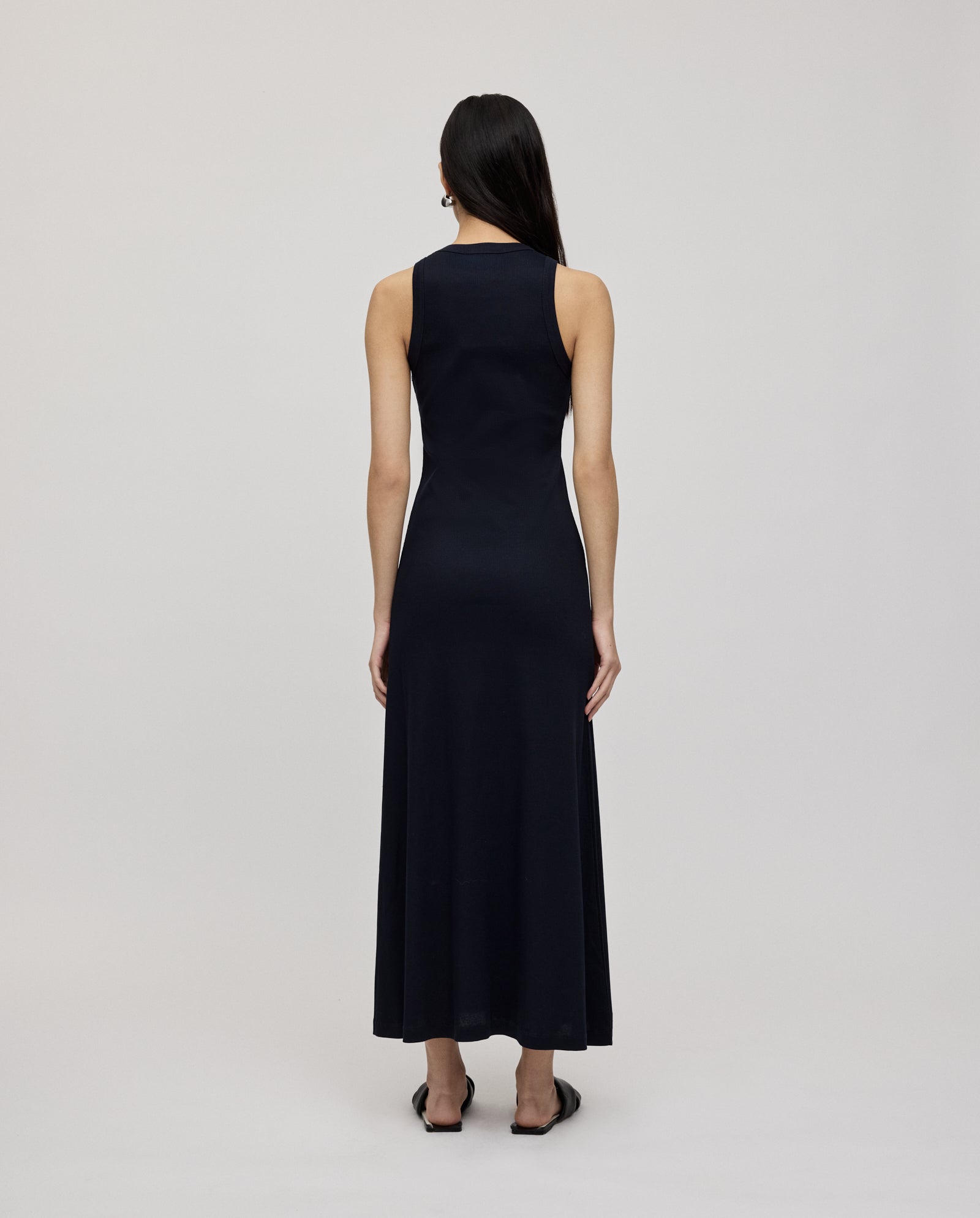 A woman, seen from behind against a plain light background, wears the IVY OAK KRISTYNA Dress—a long, sleeveless black dress with a flared skirt.