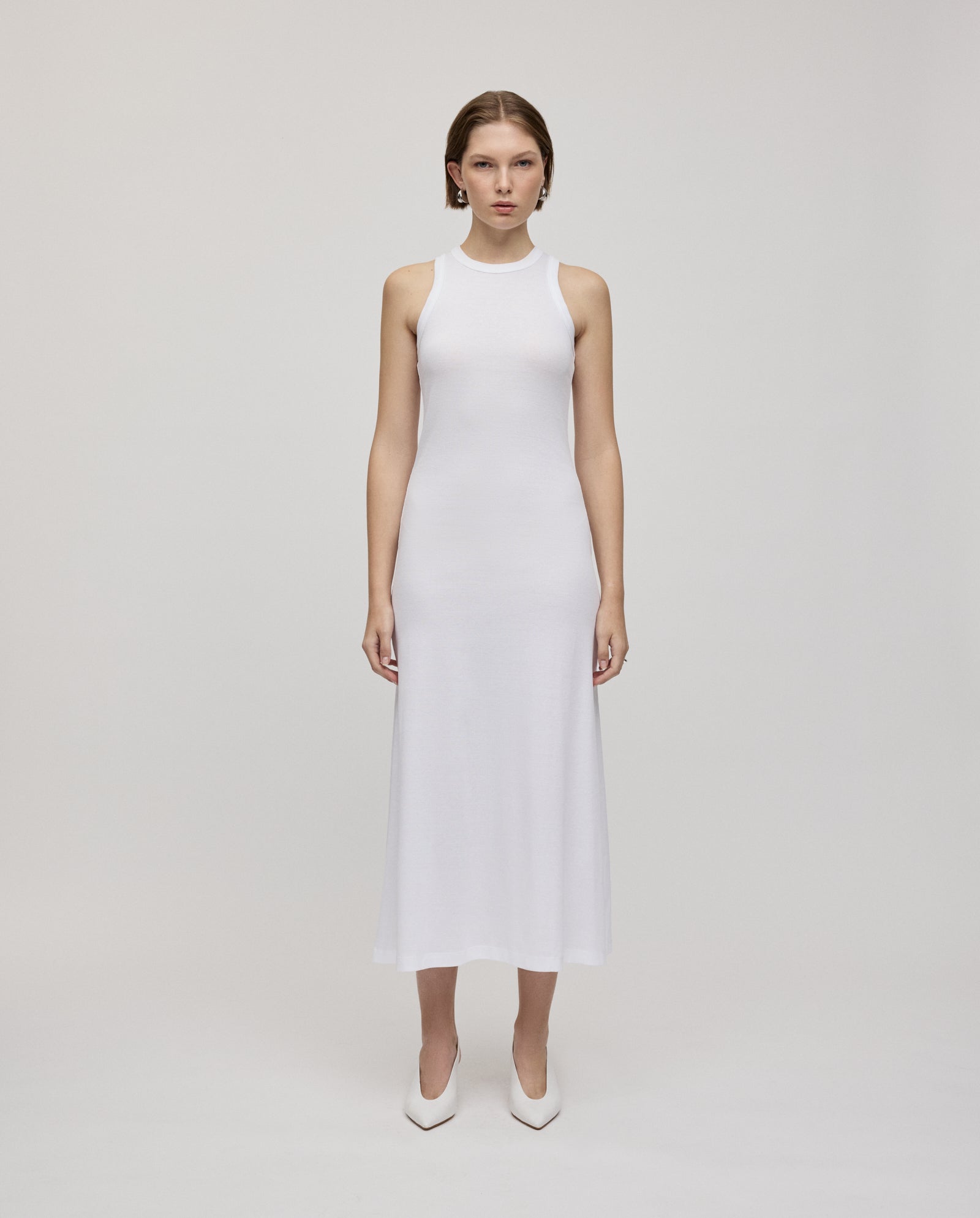 A woman in the IVY OAK KRISTYNA sleeveless, ankle-length dress with a flared skirt and white heels stands against a plain light background.