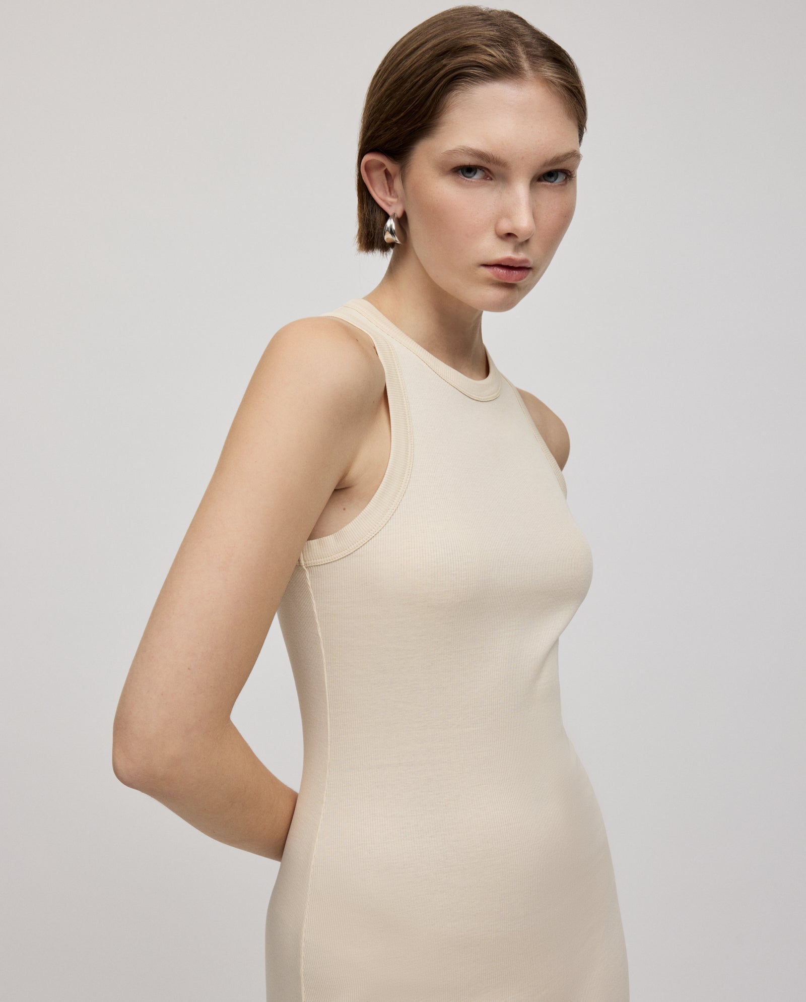 A woman with short hair wears the IVY OAK KRISTYNA sleeveless, fitted ribbed knit dress, standing against a plain light background.