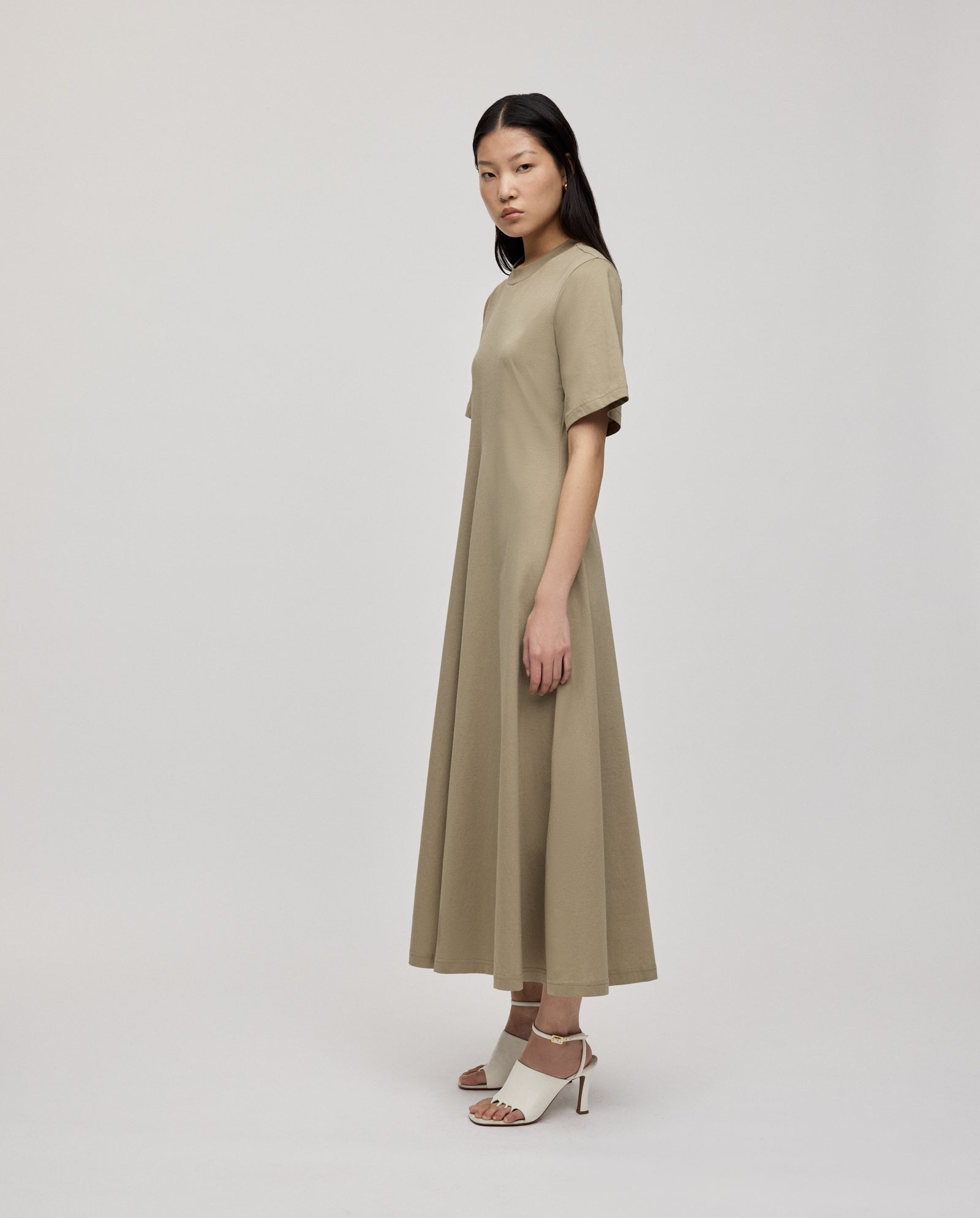 A woman in a beige IVY OAK FRANZISKA Jersey Dress with a fitted silhouette and heeled sandals stands against a plain background.