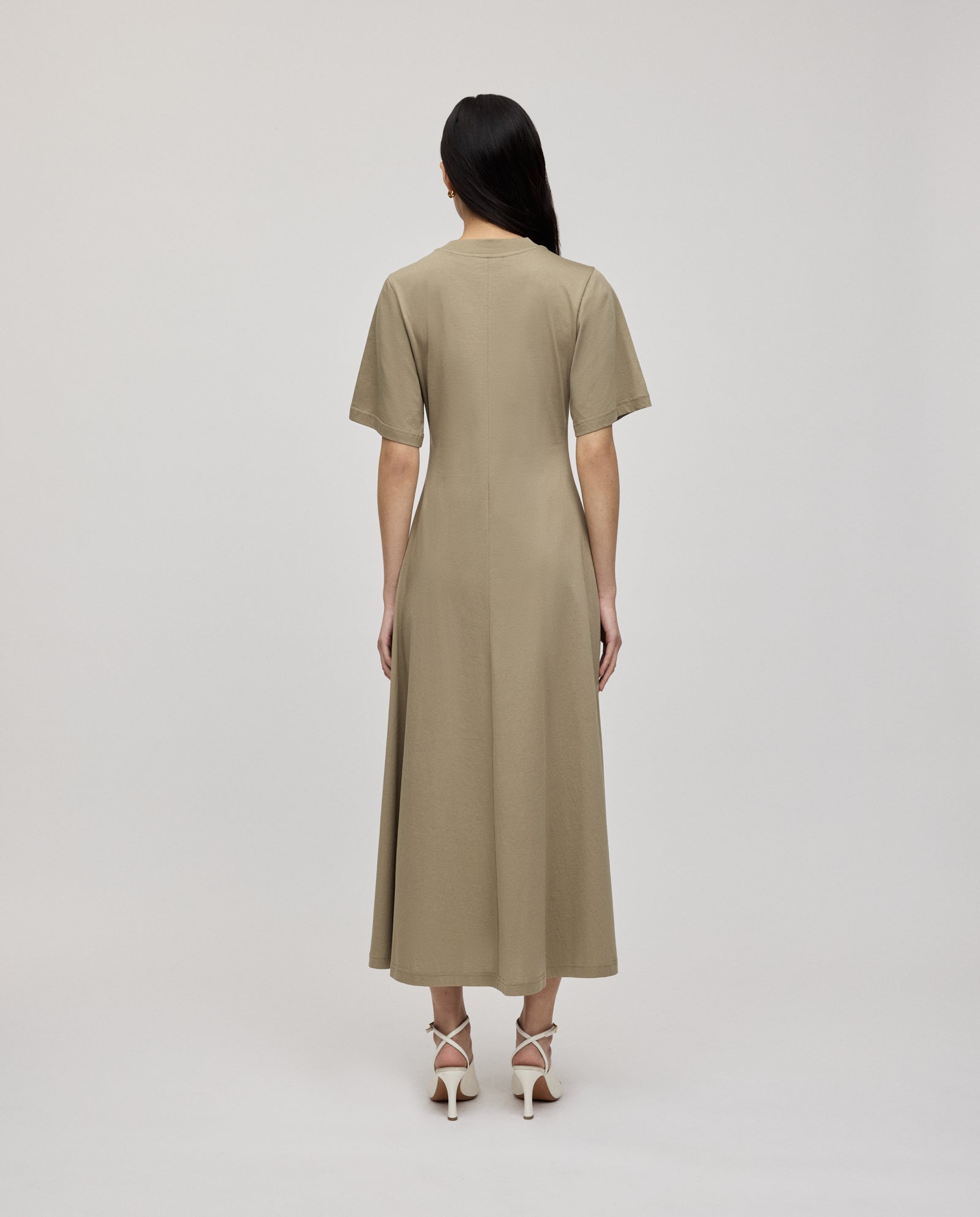 Woman in a beige IVY OAK FRANZISKA Jersey Dress with a fitted silhouette and white heels, standing with her back to the camera.