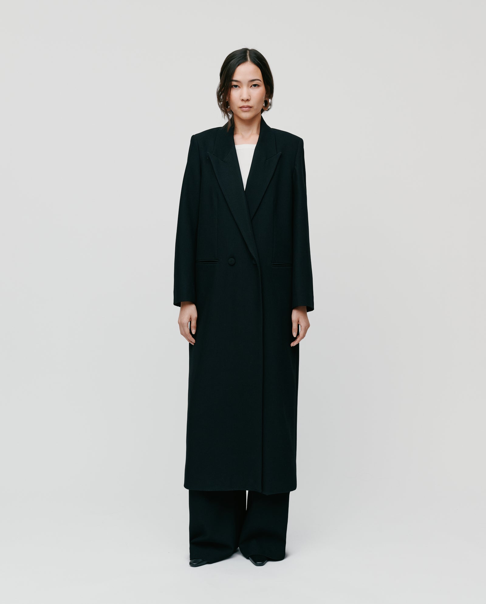 A woman showcases transformable style in the IVY OAK JIL ANN Coat and wide-leg black pants, standing against a plain white background.