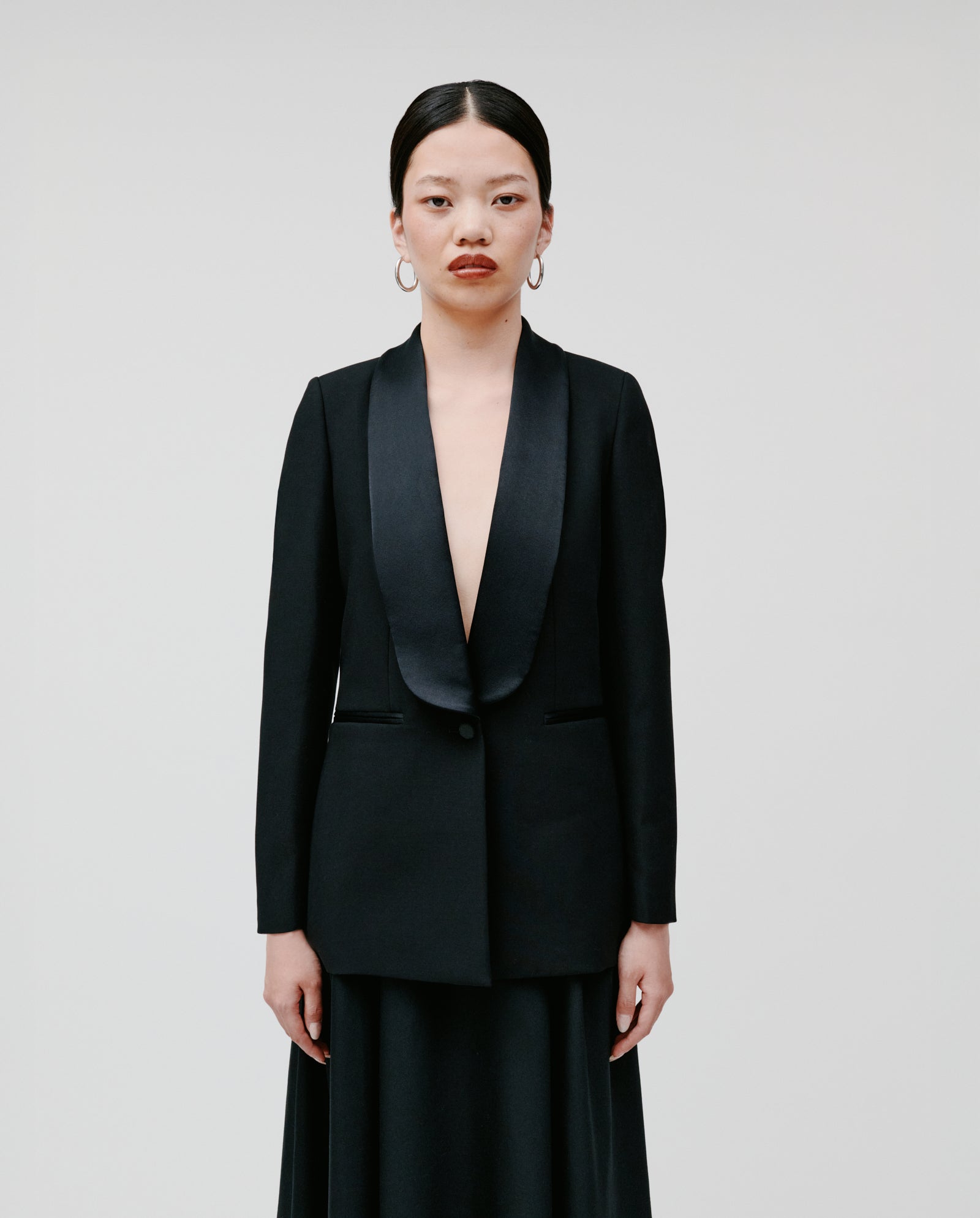 A woman in the IVY OAK JANA Blazer with a shawl collar and skirt stands against a plain white background, looking at the camera.