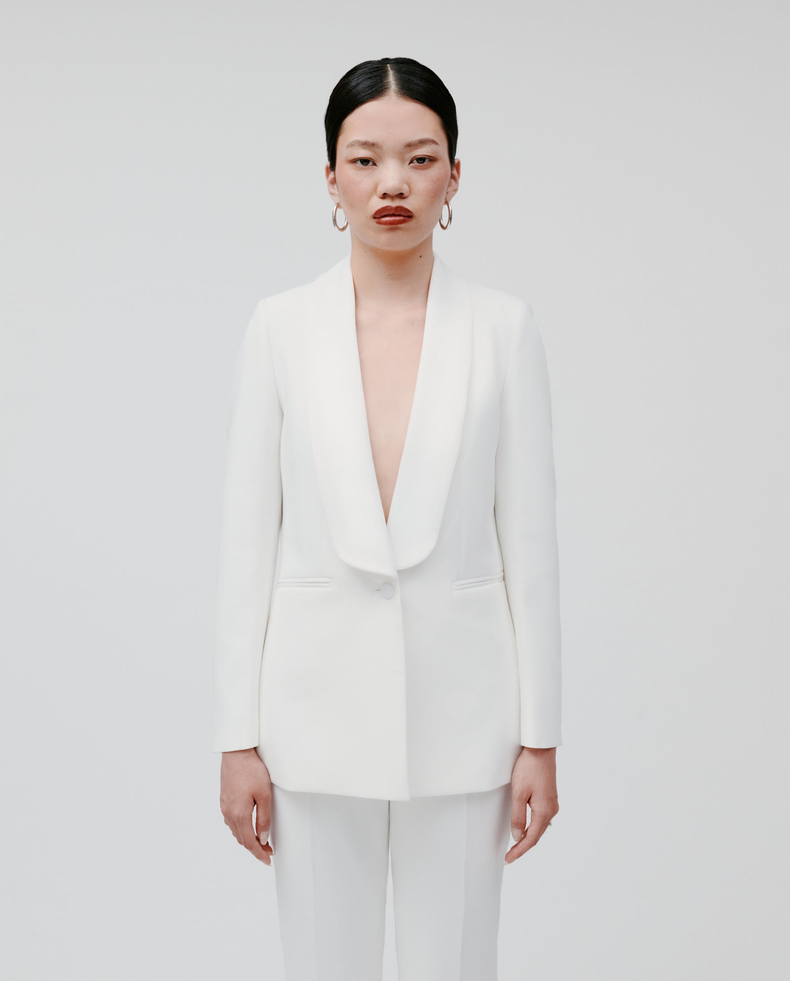 A woman wears the IVY OAK JANA Blazer—a white, lined blazer with a shawl collar—paired with matching pants, standing against a plain white background.