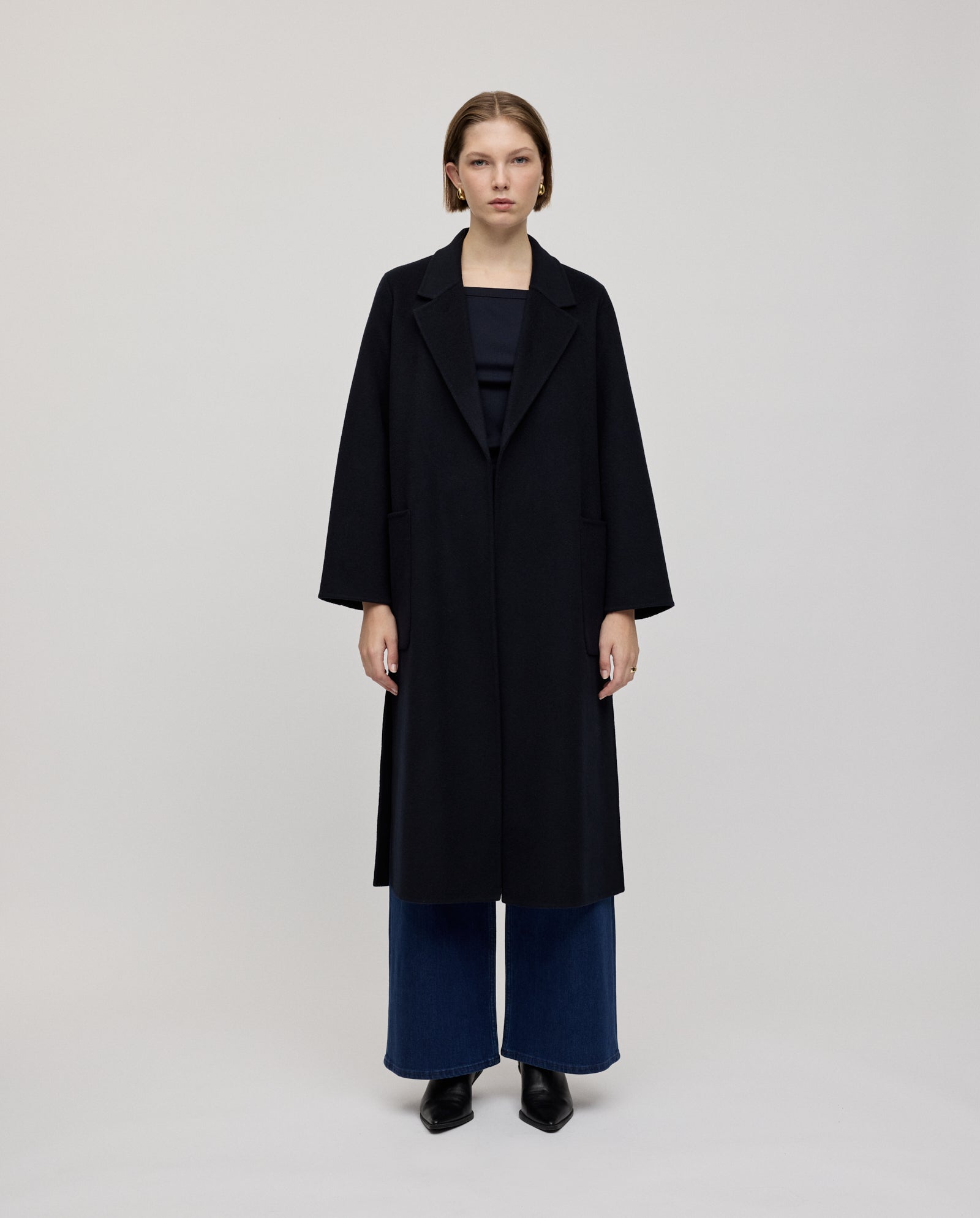 A woman wearing the IVY OAK CELIA Coat in black, paired with wide-leg jeans and black shoes, stands against a plain light background.