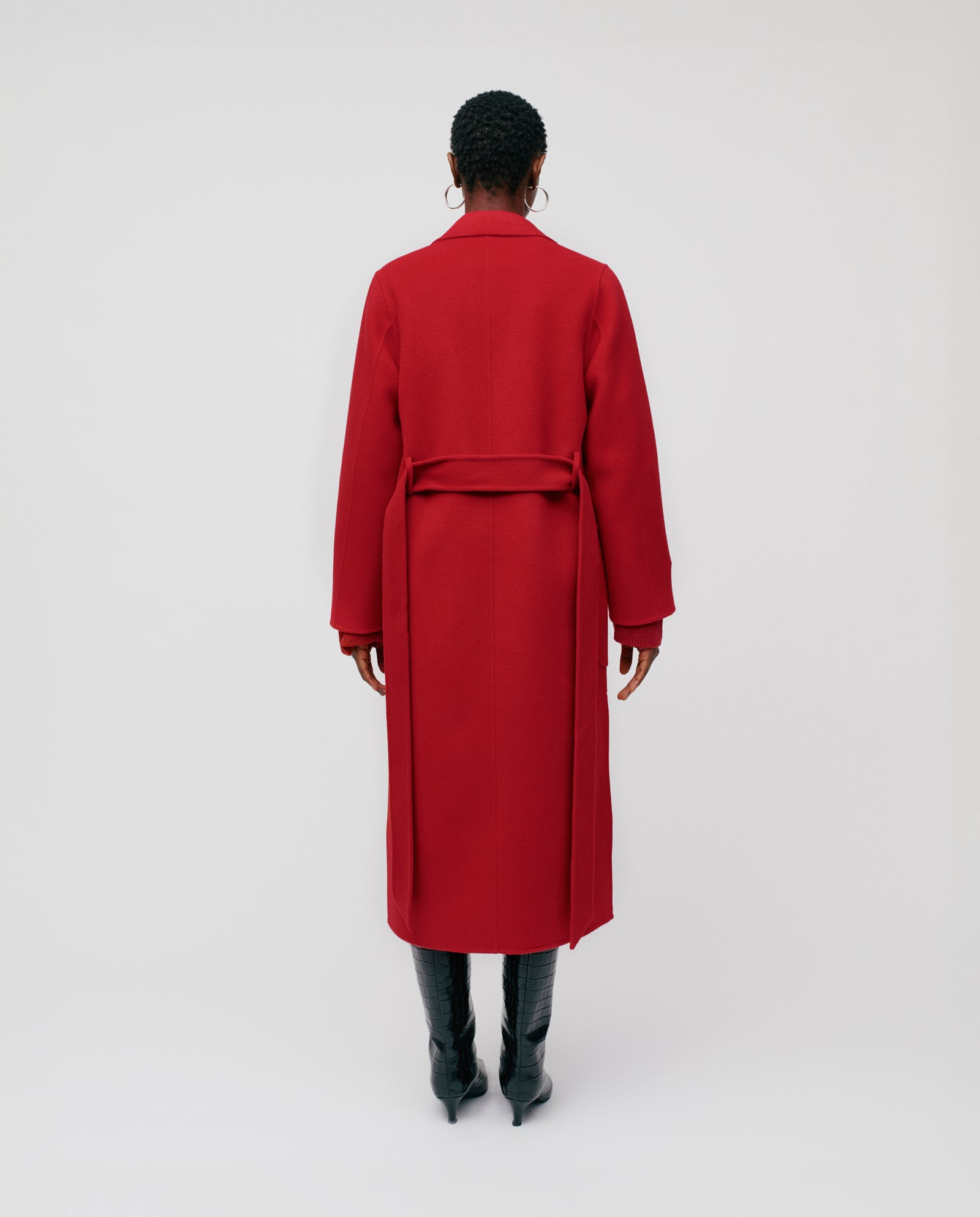 A person stands with their back to the camera, wearing the IVY OAK CELIA Coat in red wool (Responsible Wool Standard), paired with black boots against a plain background.