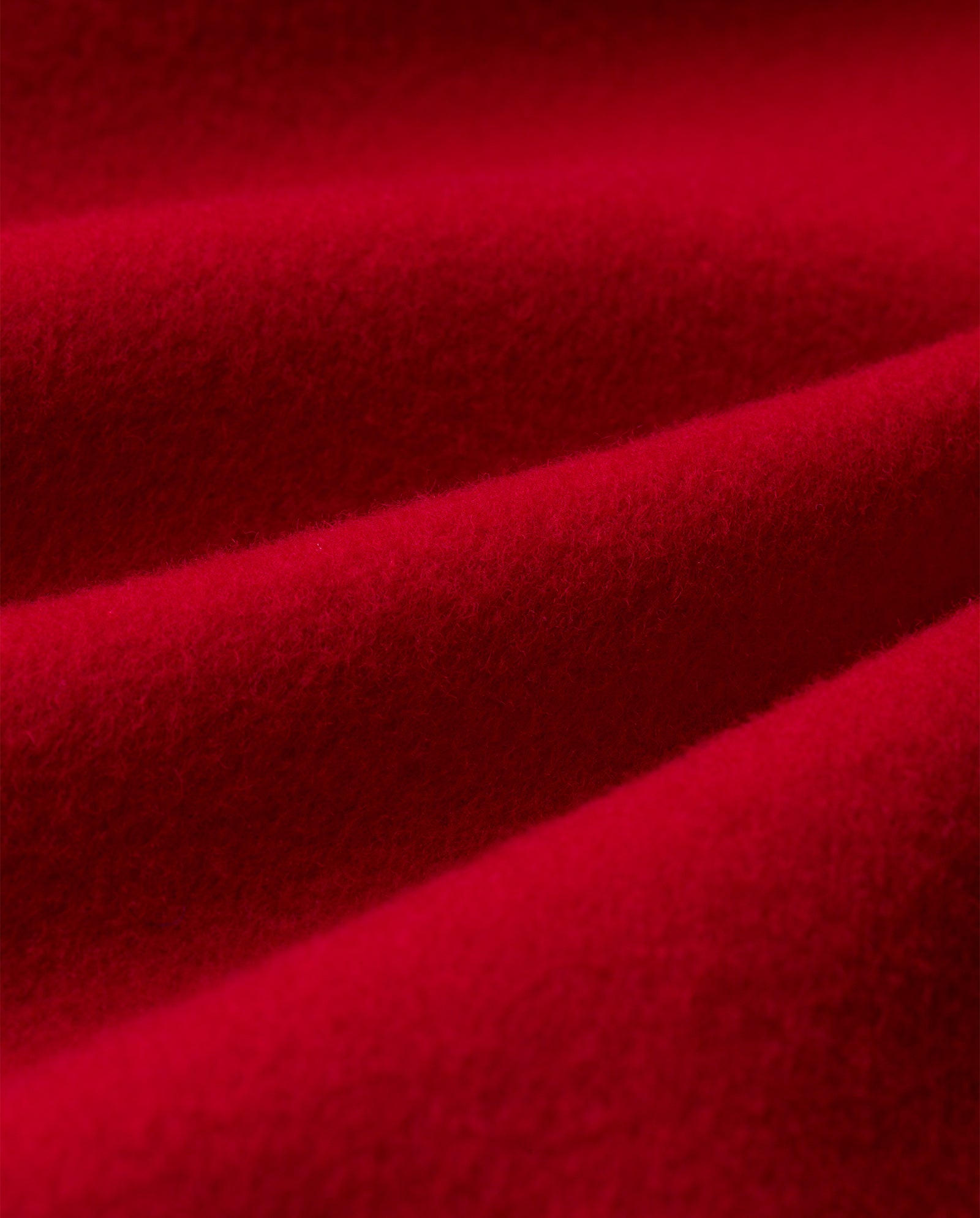 Close-up of the soft, red fabric with gentle folds and velvety texture on the CELIA Coat by IVY OAK—a luxurious midi-length design crafted from Responsible Wool Standard-certified wool.