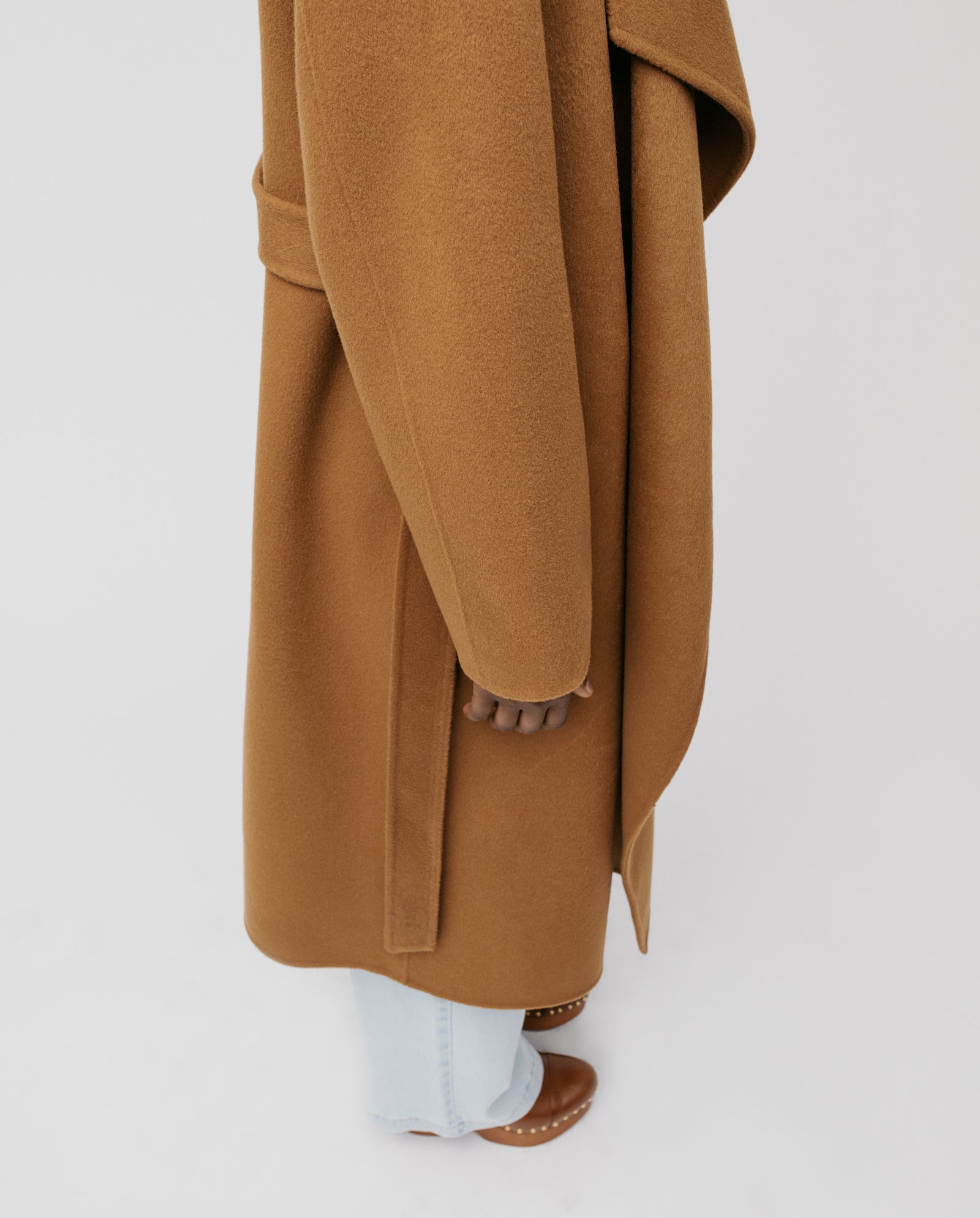 Person wearing the IVY OAK CARRIE ROSE coat featuring a minimalistic wool design with a big lapel collar in camel, paired with light blue jeans and brown shoes on a white background.