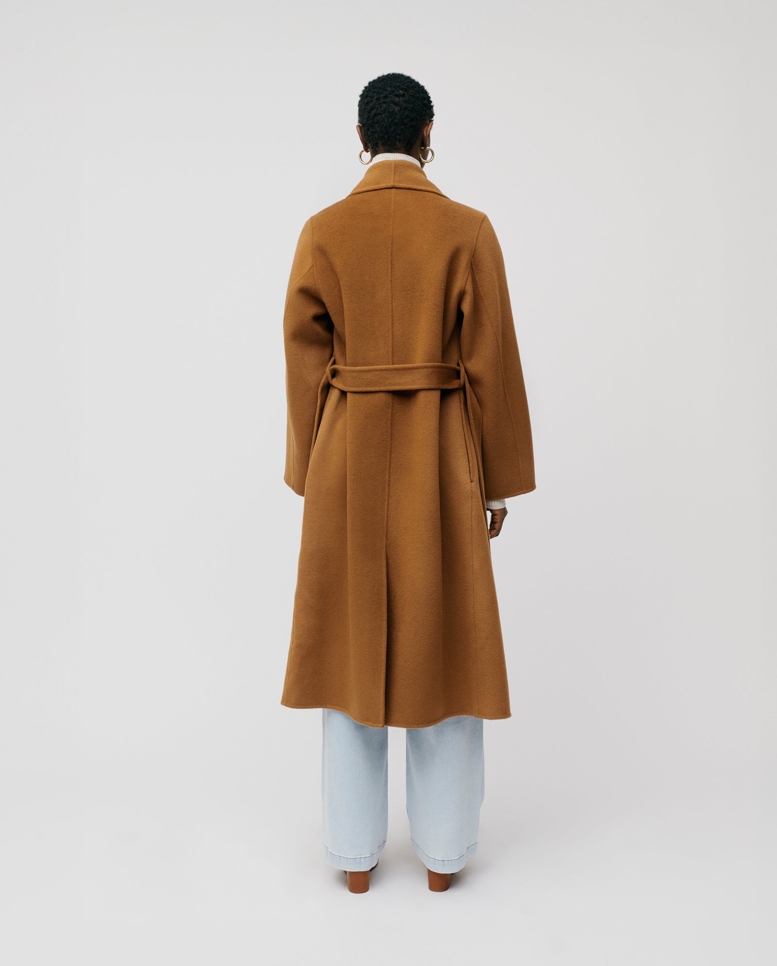 A person wearing the IVY OAK CARRIE ROSE Coat, featuring a minimalistic design with a large lapel collar, paired with light blue jeans, stands with their back to the camera.