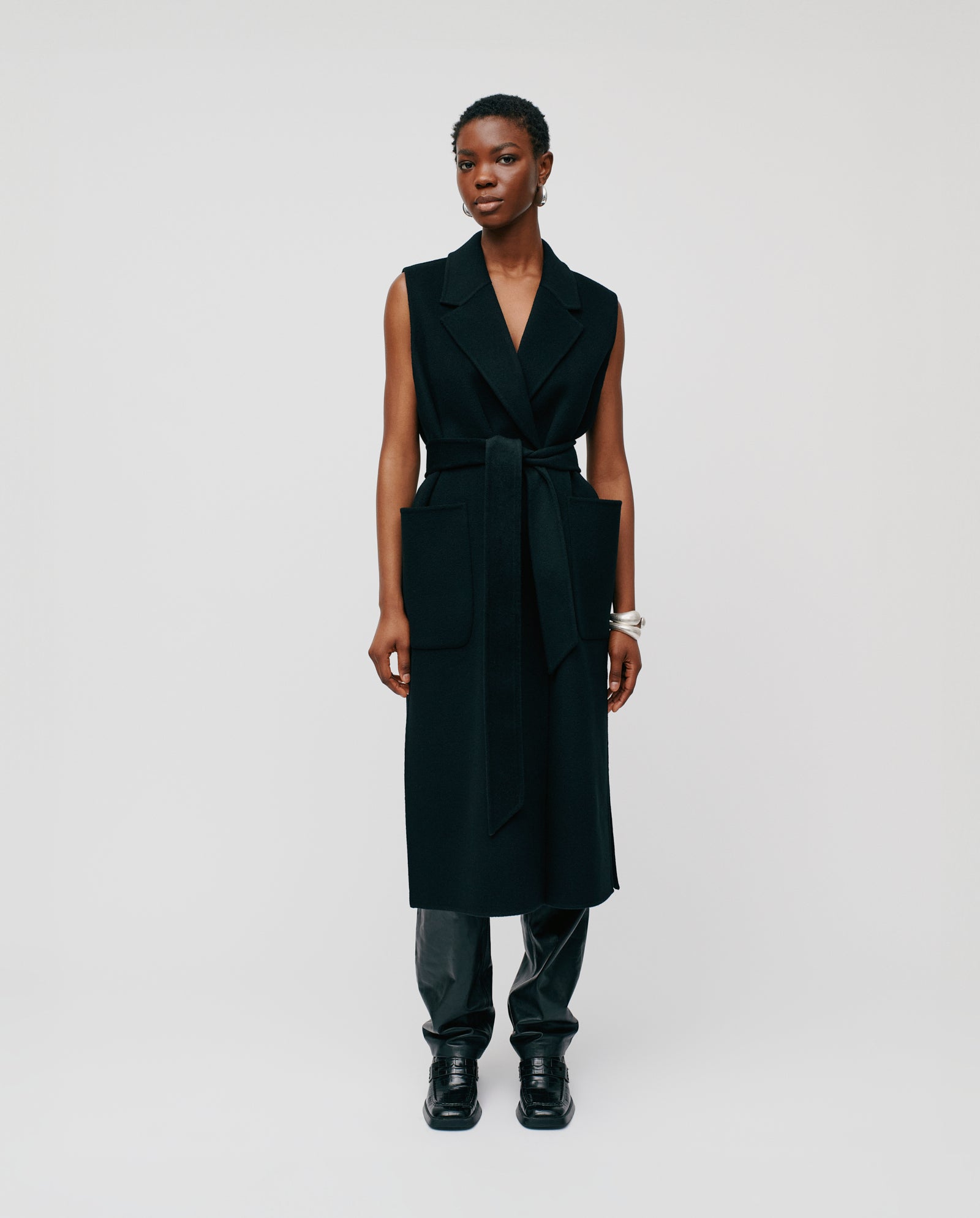 A person wears a sleeveless black CLARISSA Vest by IVY OAK (DE), made from RWS wool, over black pants and shoes, standing against a plain background.