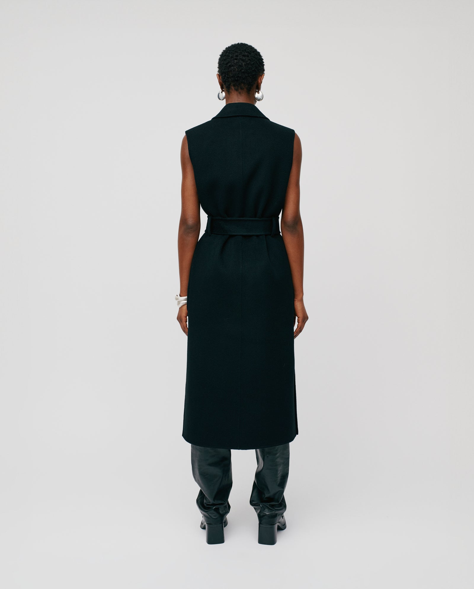A person faces away, wearing the sleeveless black CLARISSA Vest by IVY OAK (DE) in RWS-certified wool with black pants, standing against a plain background.