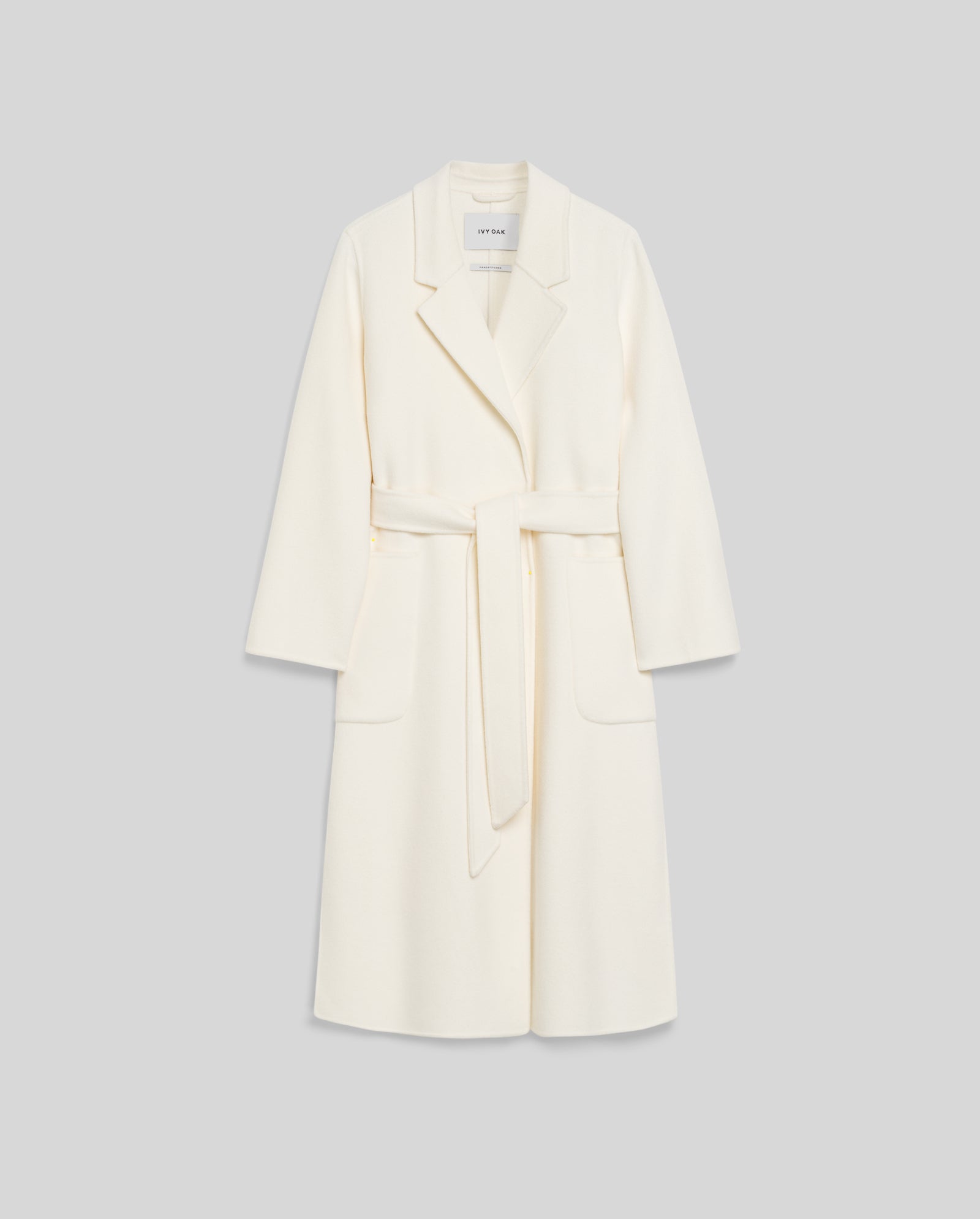 The IVY OAK CELIA Wool Coat is cream-colored with a belt, loose fit, wide lapels, and large front pockets, displayed on a light gray background.
