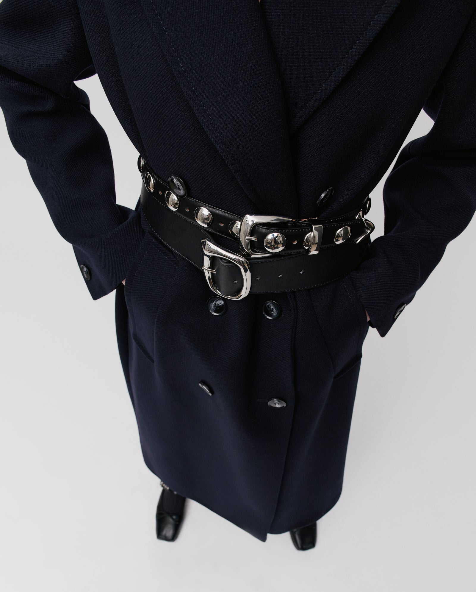 Person wearing the IVY OAK CLEMENCE Coat, an oversized winter coat with a wide, studded black belt and hands in pockets, seen from above.