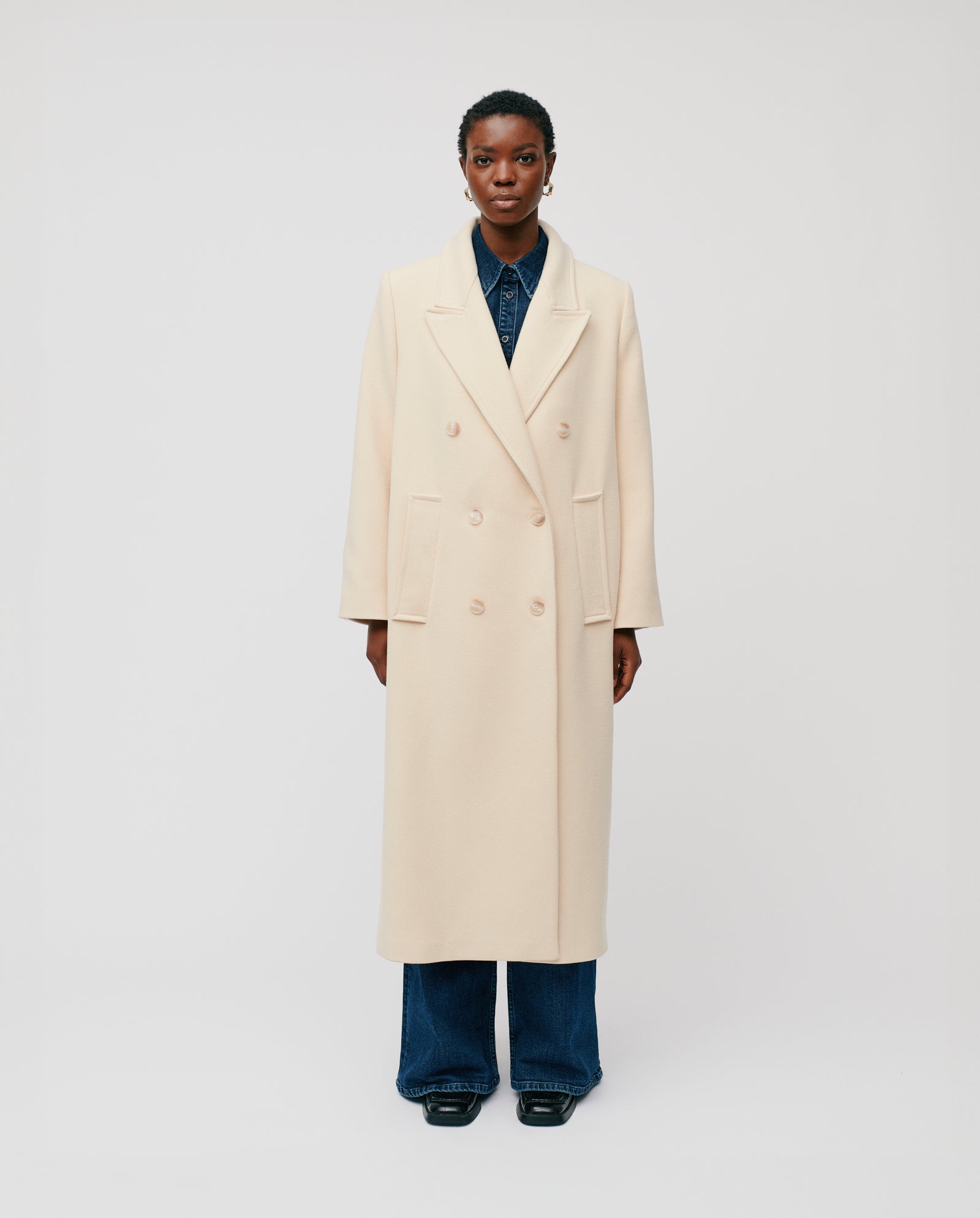 A person wears the IVY OAK CLEMENCE Coat, an oversized boxy winter coat in a luxury Virgin Wool blend, styled double-breasted over a dark shirt and wide-leg jeans against a plain background.