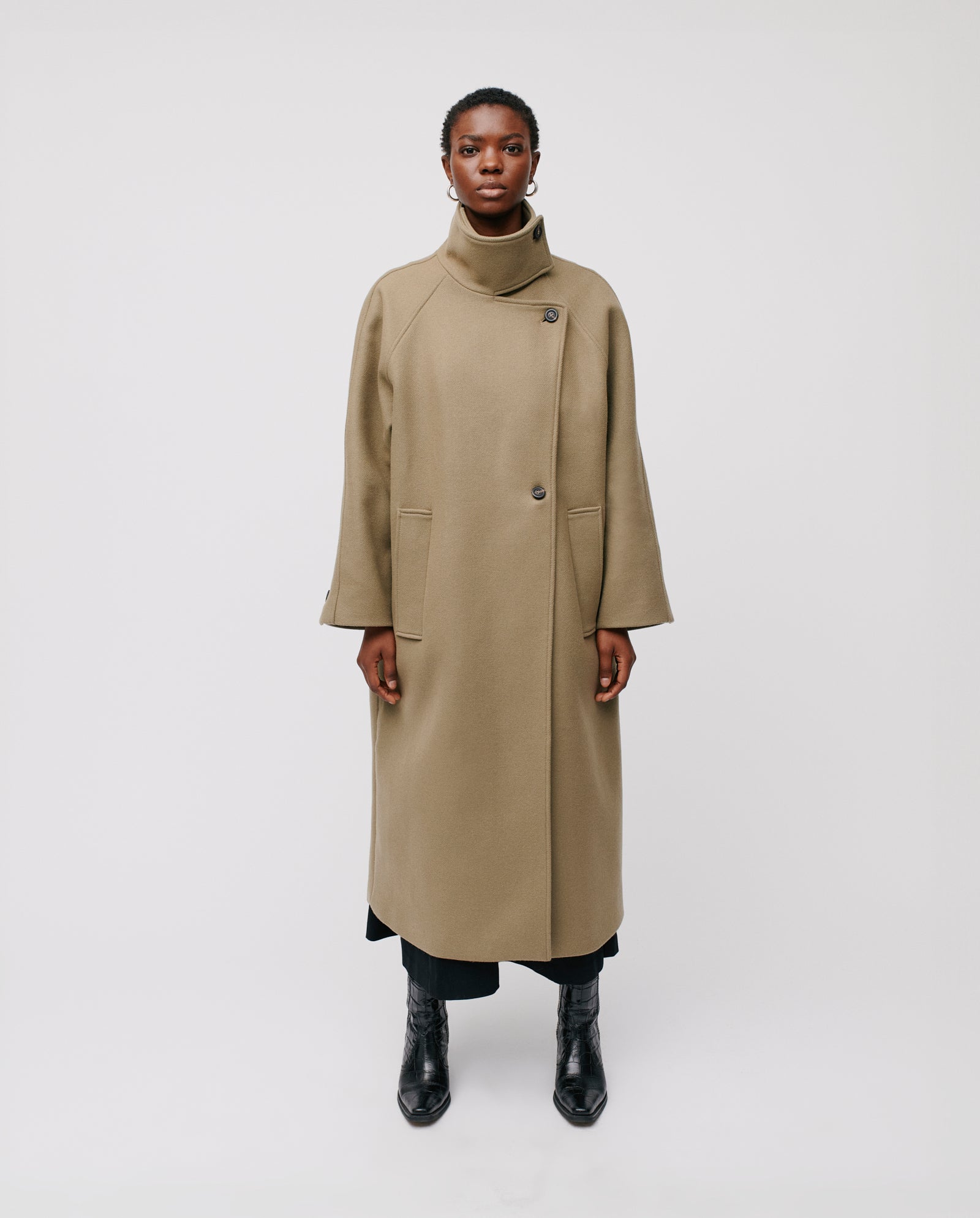Model wearing the CLEO Coat by IVY OAK, featuring an oversized fit with raglan sleeves and a high stand-up collar, paired with black pants and boots against a white background.