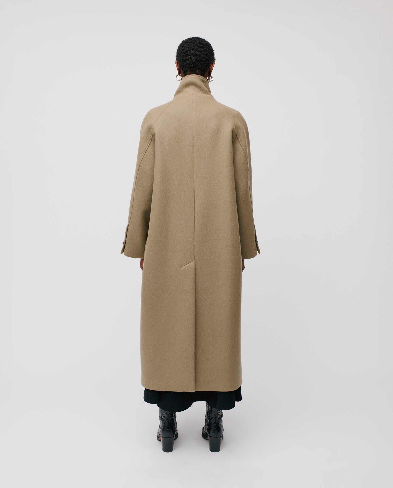 A person stands with their back to the camera, wearing the IVY OAK CLEO Coat—an oversized caban style with a high stand-up collar—paired with black boots against a plain background.