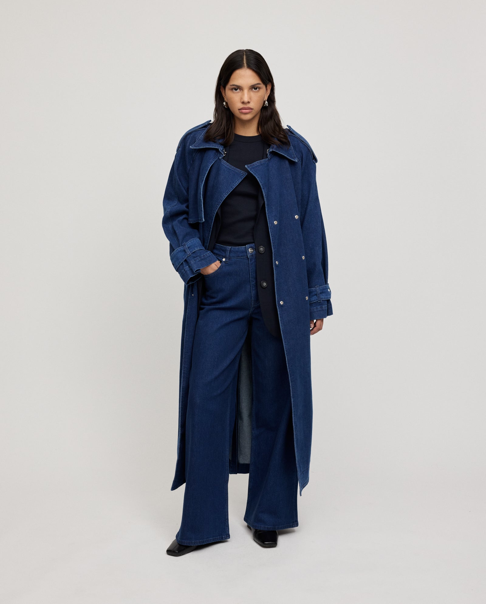 A woman wears the IVY OAK CORDELIA Coat with an adjustable belt and wide-leg jeans, posing against a plain light background.