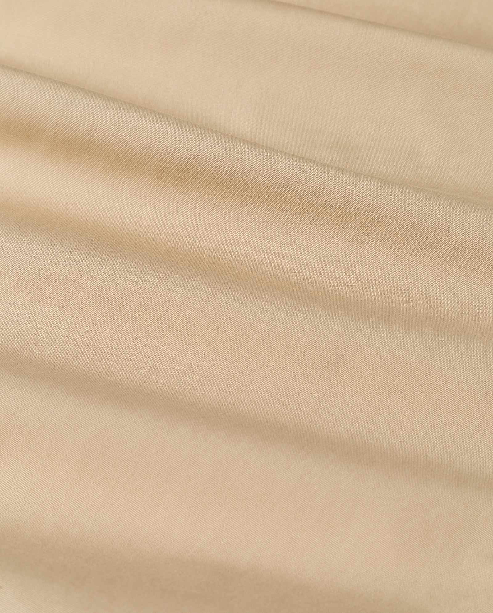 Close-up of beige fabric with soft, diagonal folds and a smooth texture, inspired by the elegance of the CLEMENTINE Coat by IVY OAK.