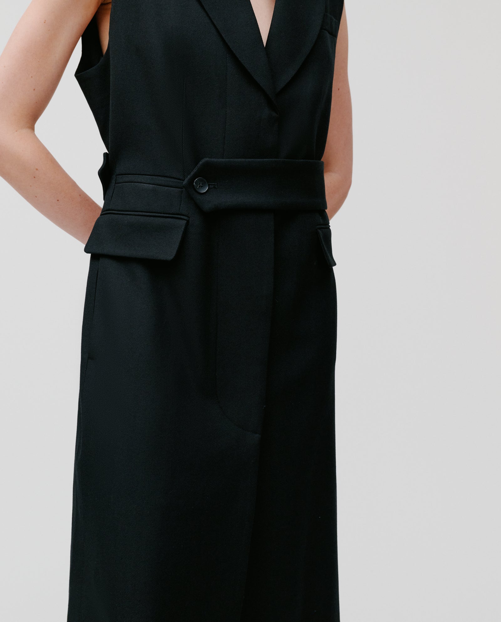 A person models the IVY OAK CORI ANN Vest, a sleeveless black tailored dress featuring lapels, flap pockets, and a velvet collar, standing against a plain background.