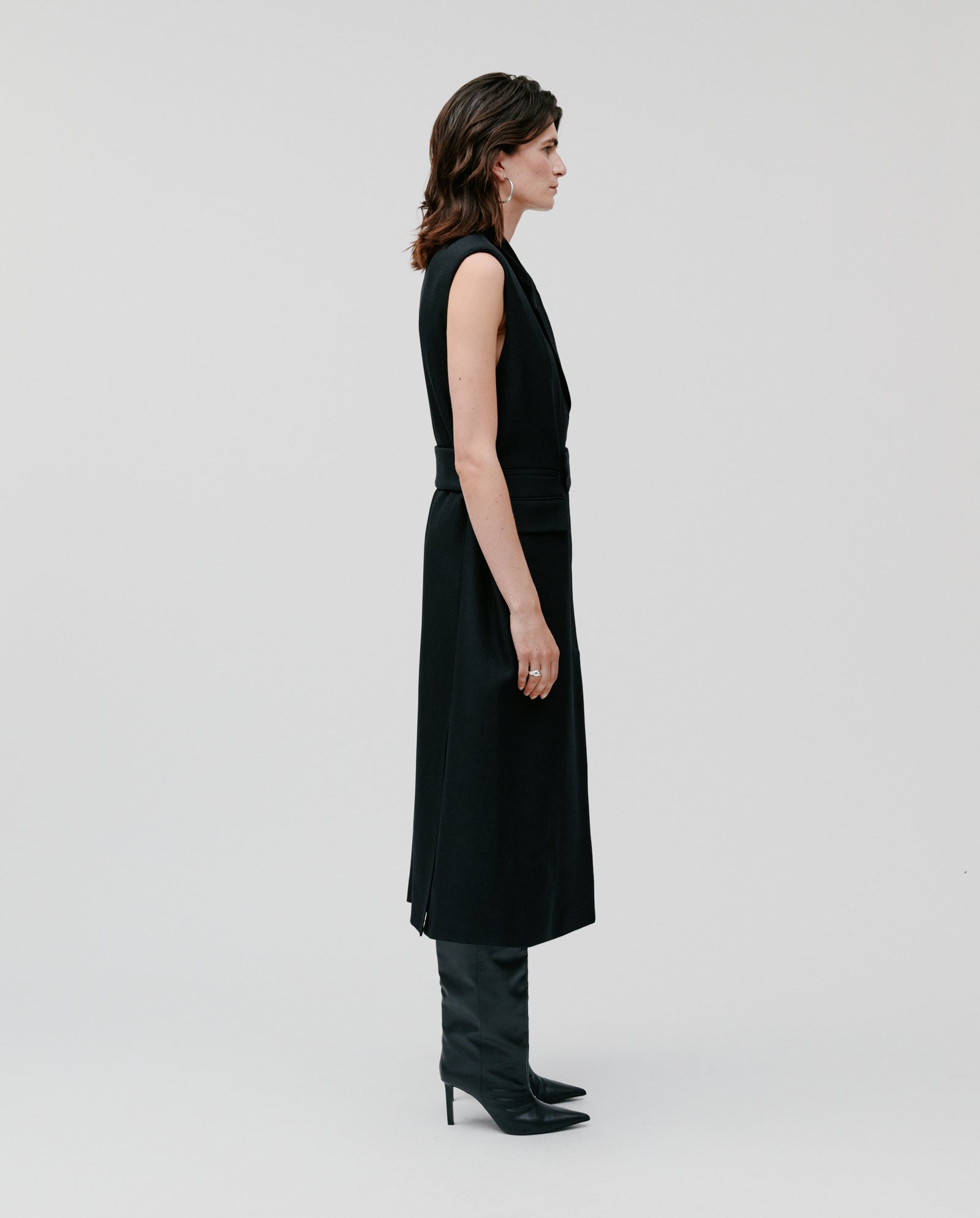Woman in a sleeveless black dress, styled with the IVY OAK CORI ANN Vest featuring a velvet collar, and black heeled boots, standing in profile against a plain background.