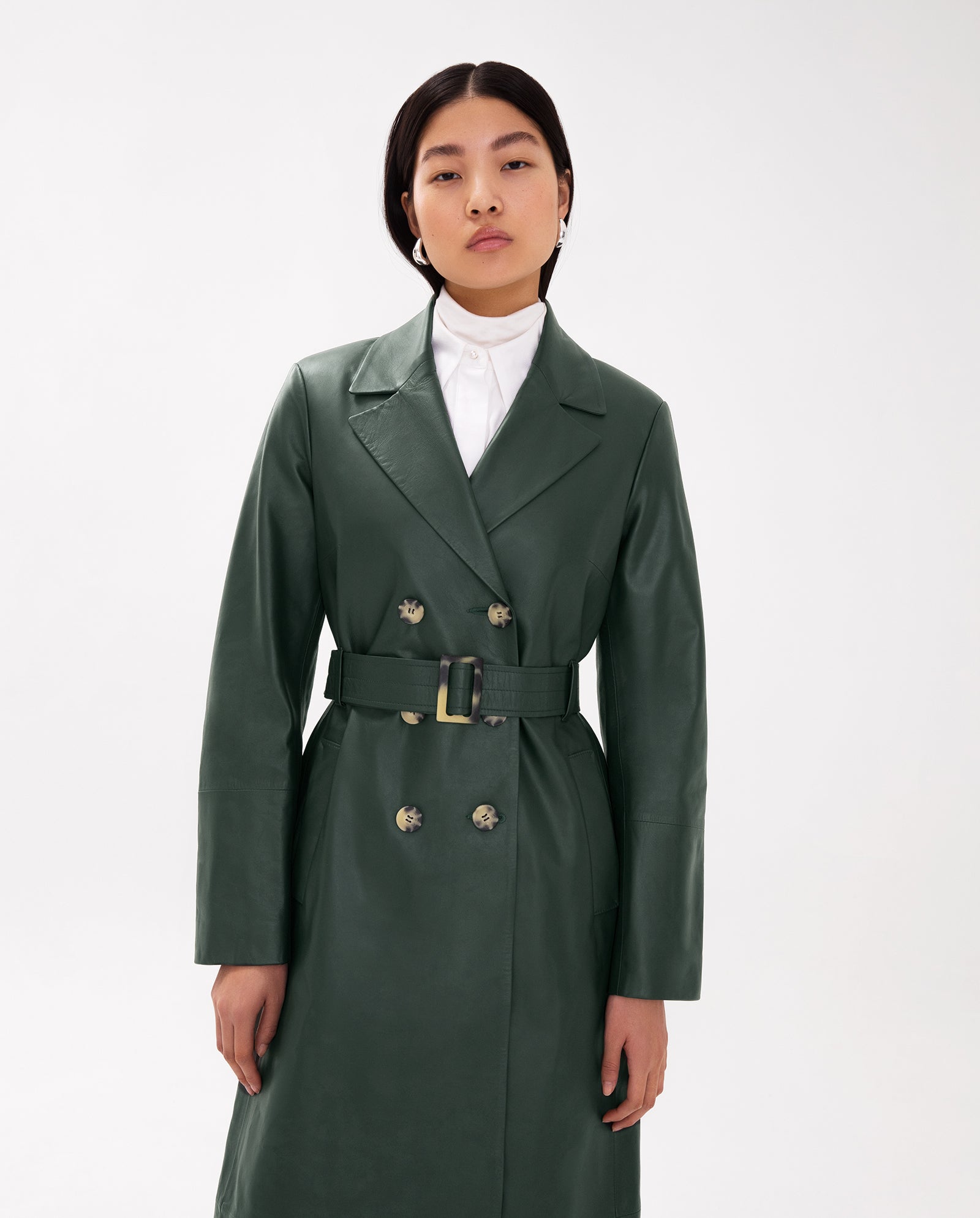 A woman wearing the IVY OAK LIONNE Coat in green Lamb Nappa leather at midi length over a white collared shirt, standing against a plain white background.