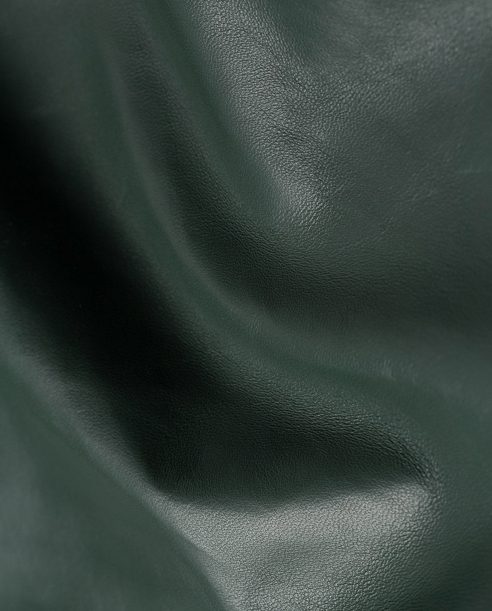 Close-up of dark green, slightly wrinkled Lamb Nappa leather with a soft sheen, featured on the luxurious LIONNE Coat by IVY OAK.