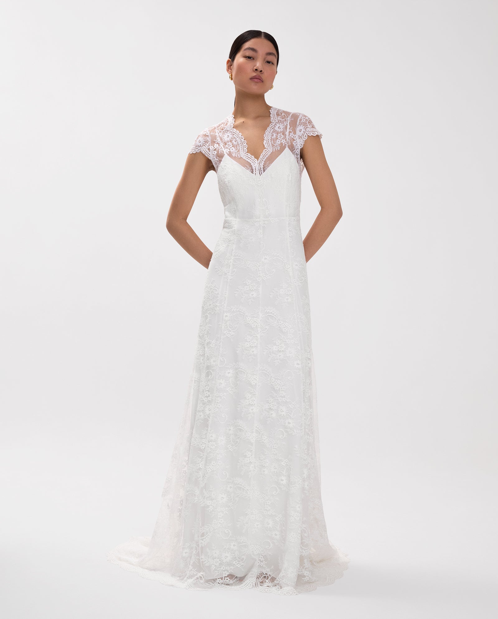 A woman models the IVY OAK DANIELLA ROSE Bridal Dress—an elegant white lace gown with cap sleeves and an eyelash neckline—against a plain white background.