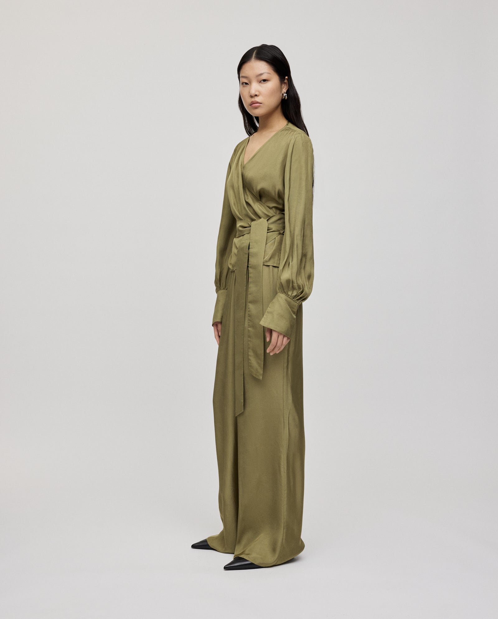 Woman wearing the ELOISE Top by IVY OAK, a long-sleeved olive green organza wrap top with wide cuffs and a long belt, standing against a plain background.