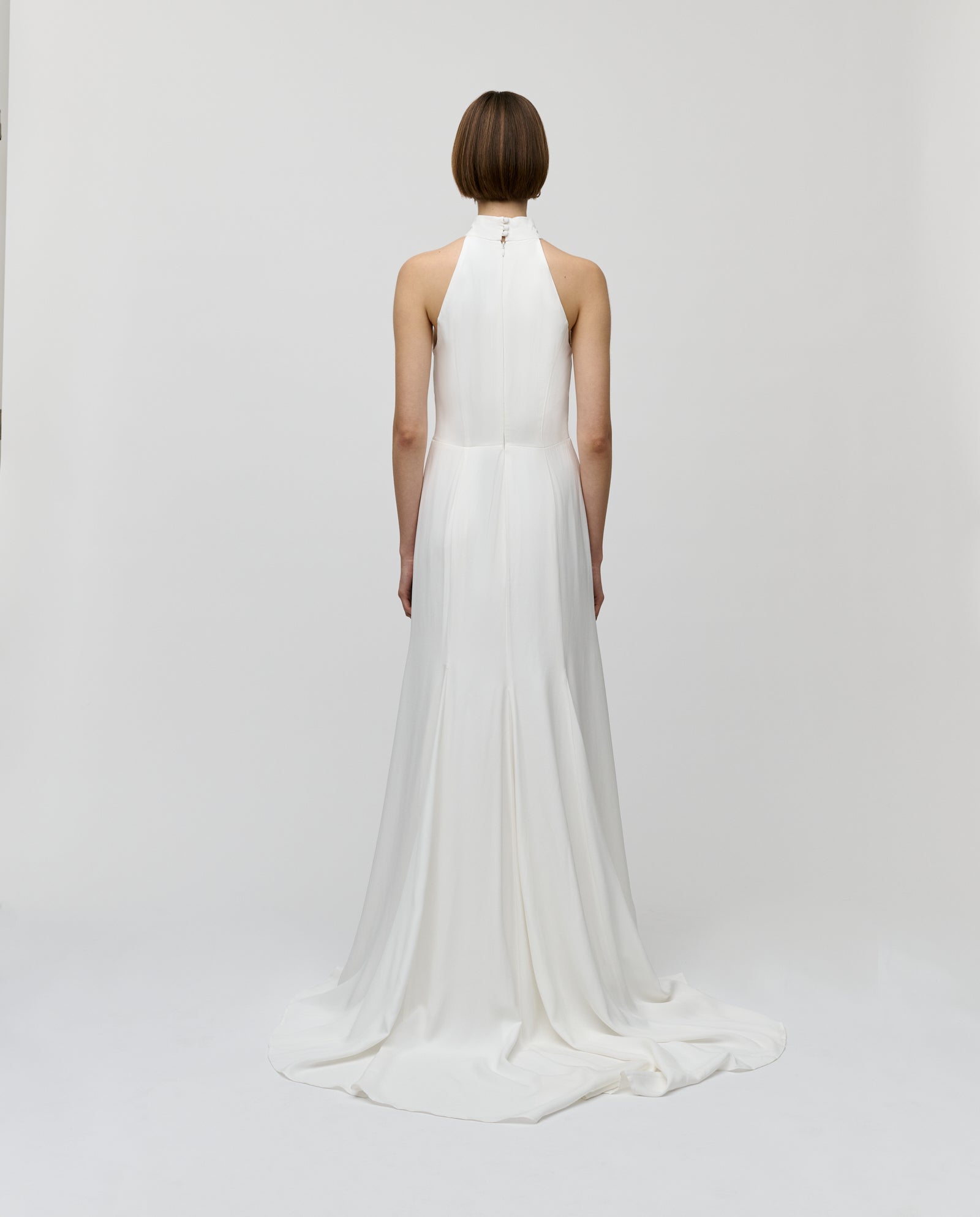 A woman faces away, showcasing the MEREDITH Dress by IVY OAK—a sleeveless white bridal gown with a long, flowing train.