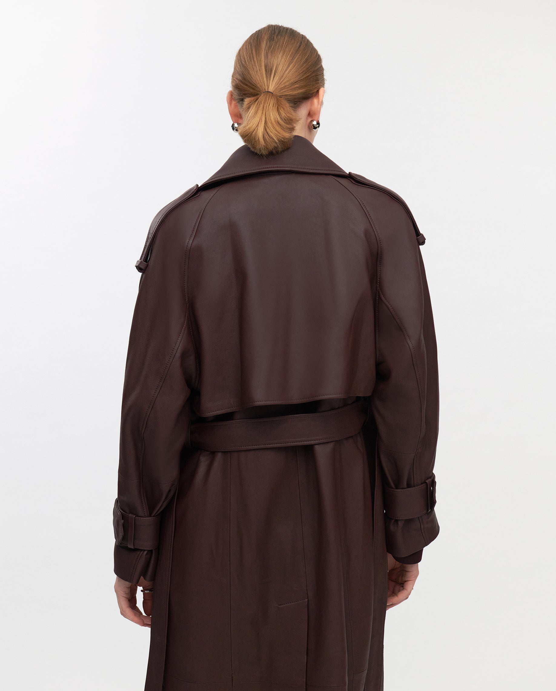 A person with blonde hair in a bun is shown from the back wearing the IVY OAK LILITH Trench, a long, dark brown belted coat.