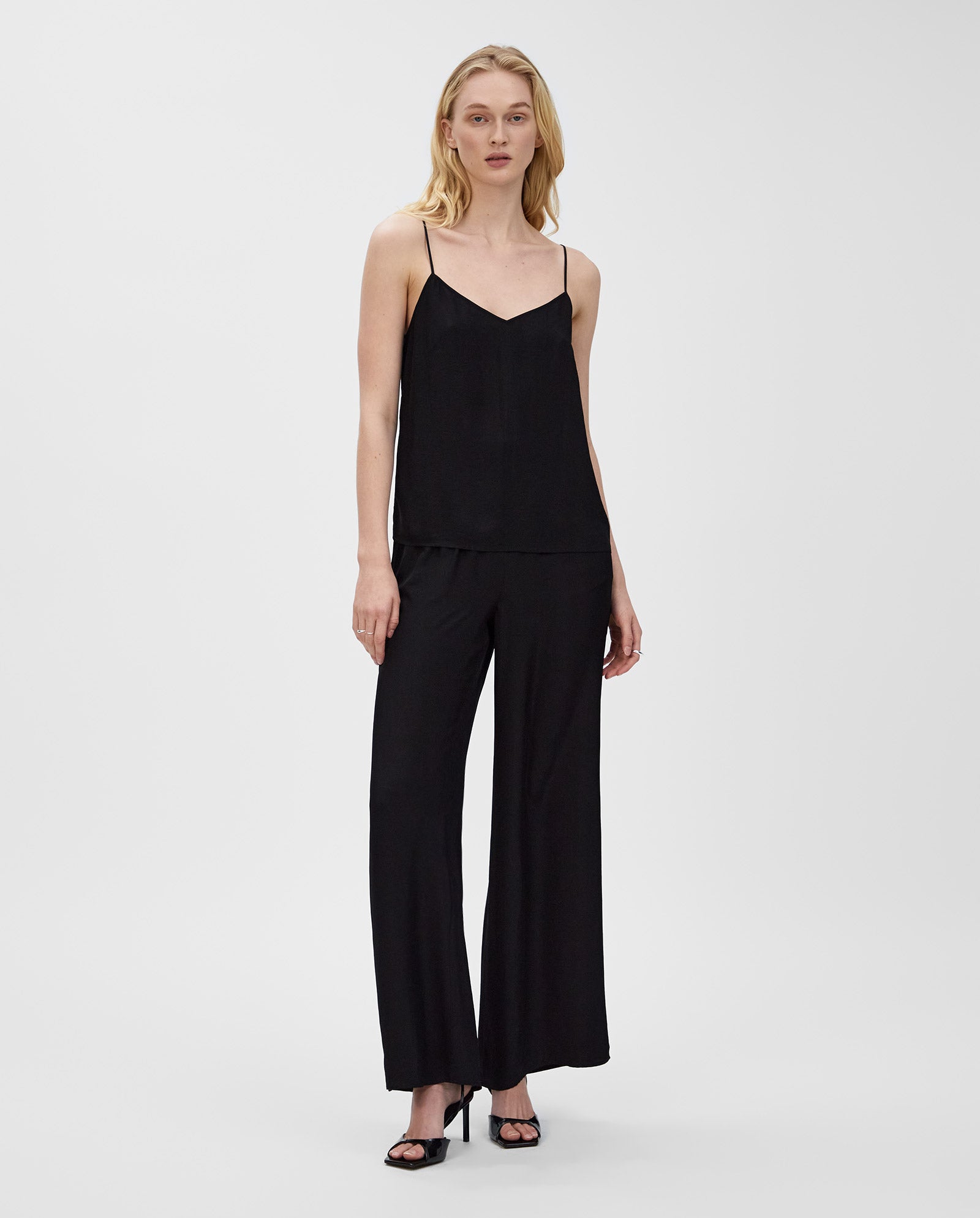 Woman in an IVY OAK TILDA ANN Top with a V-neckline, wide-leg black pants, and black high-heeled sandals.