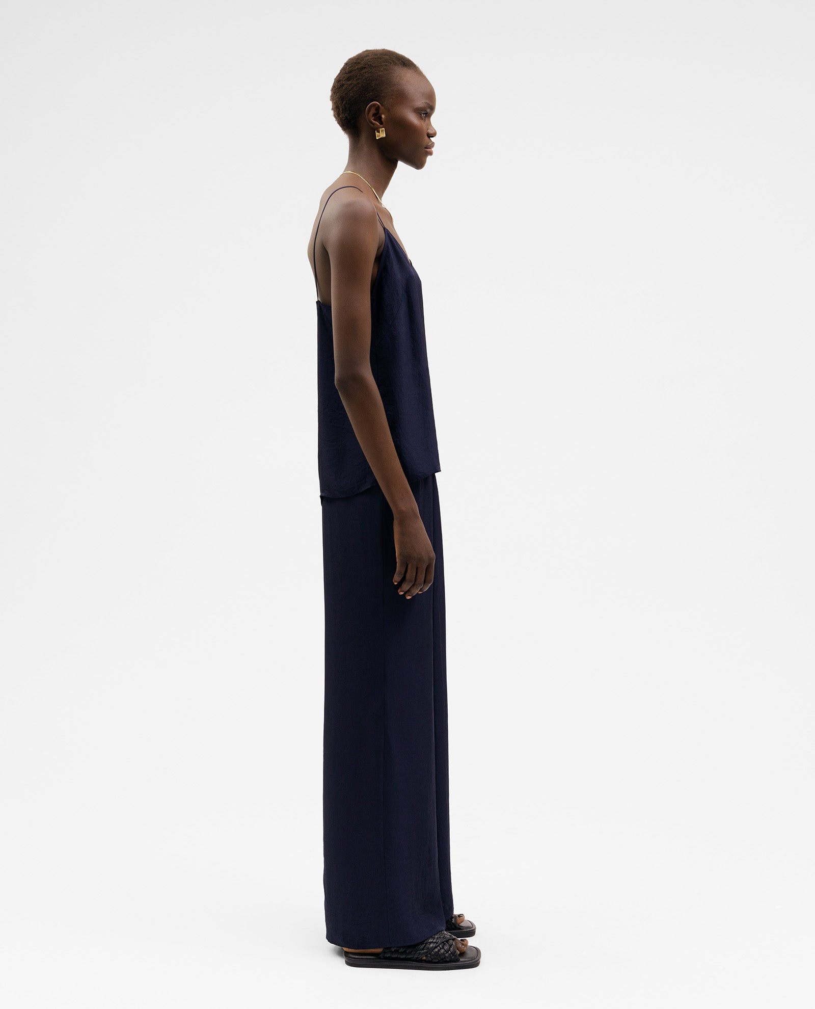 A woman stands in profile against a white background wearing the IVY OAK TILDA ANN Top with a V-neckline and matching wide-leg pants, both crafted from soft Naia acetate.