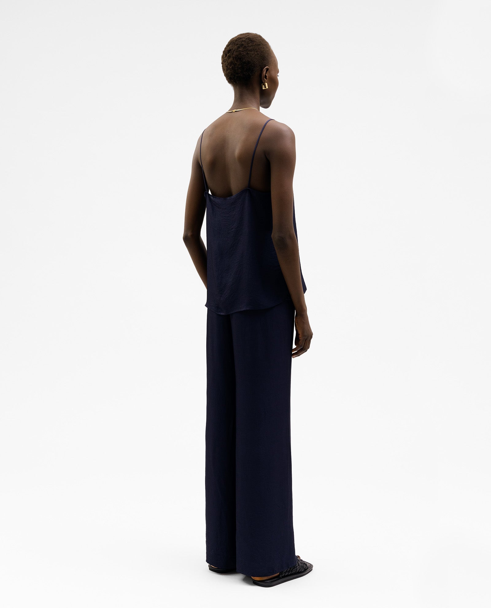 A woman faces away against a white background, wearing an IVY OAK TILDA ANN navy blue V-neck top with wide-leg pants.