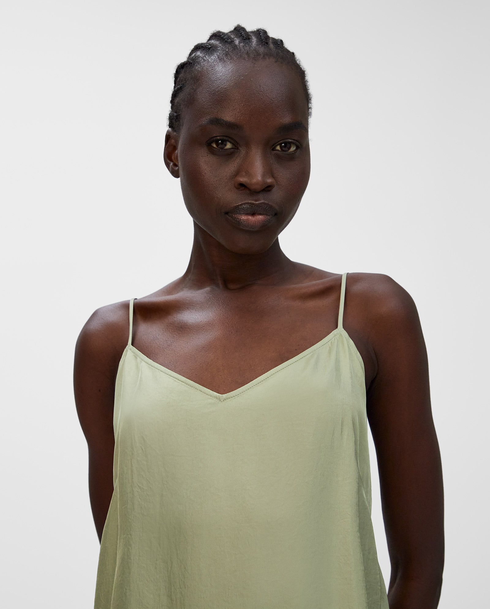 A woman wears the light green TILDA ANN Top by IVY OAK, featuring a flattering V-neckline, as she stands confidently against a plain white background.