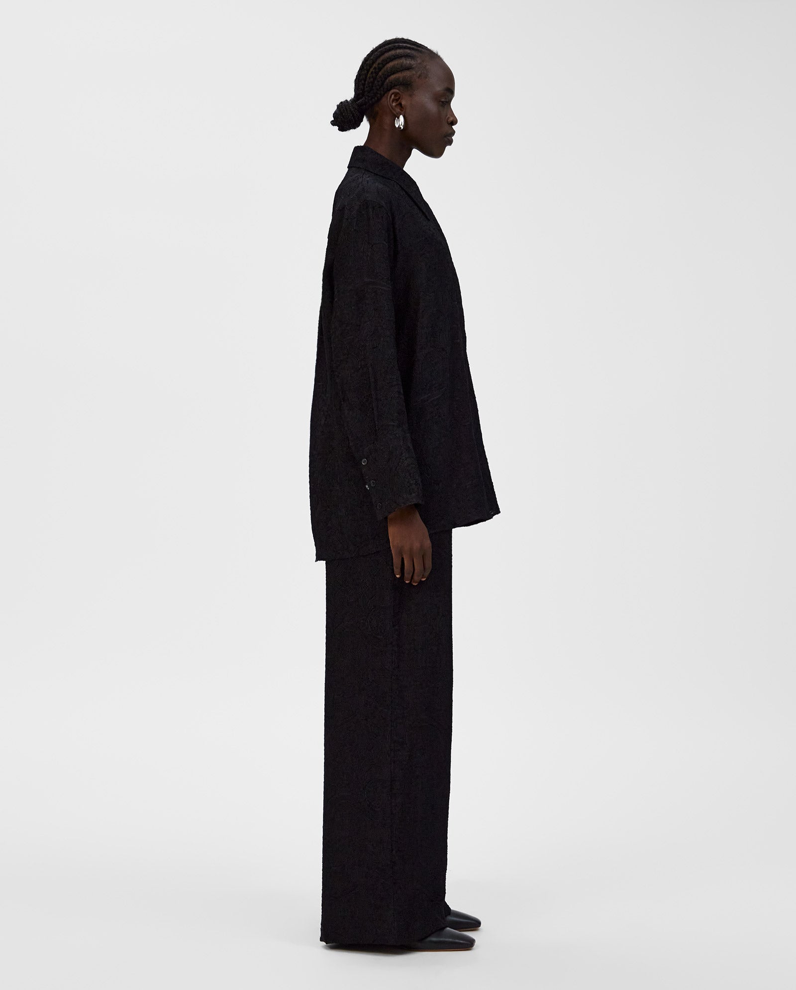 A person stands in profile against a plain white background, wearing the IVY OAK ELVIE ANN Blouse—a loose-fitting black top with a wide collar.