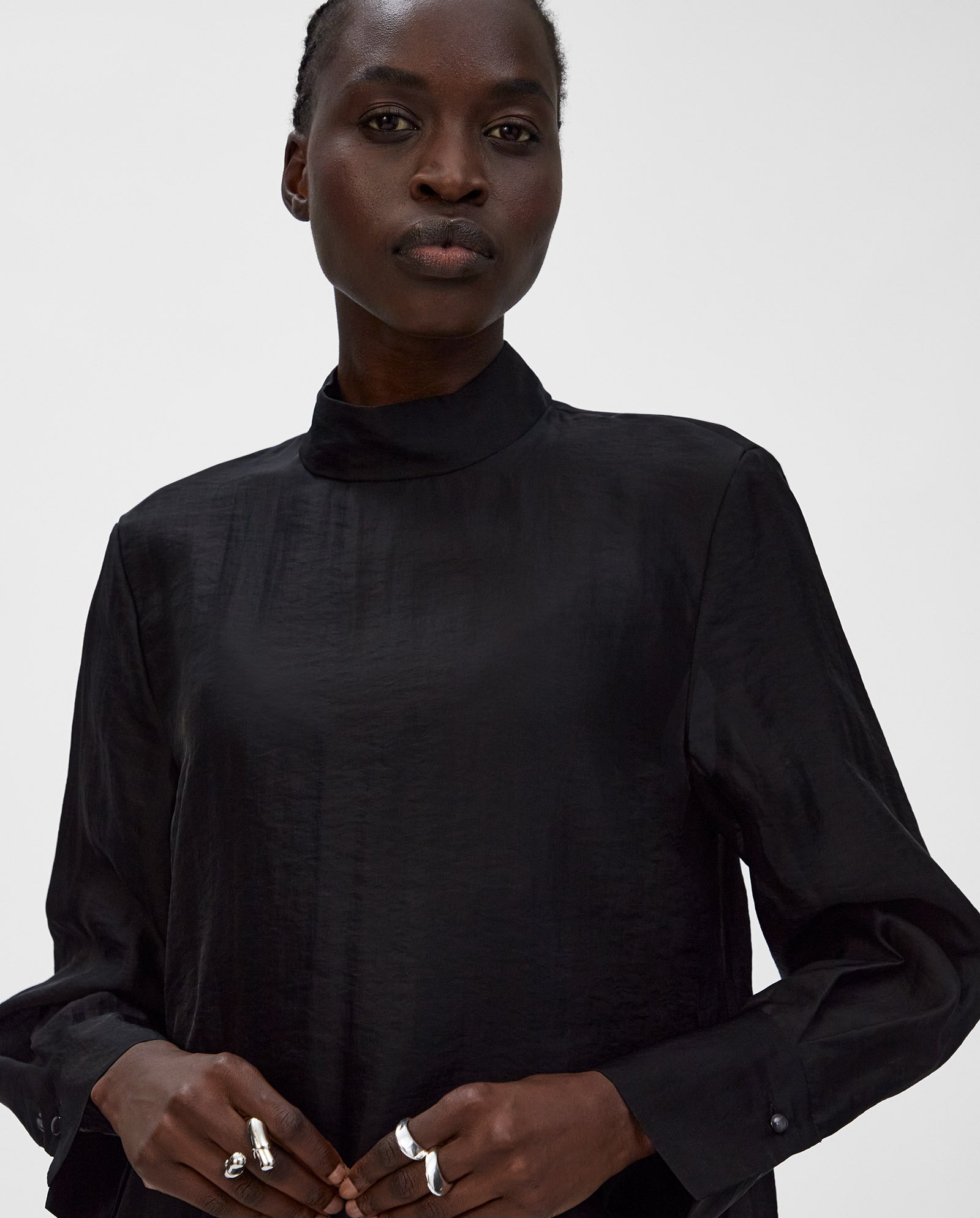 A person wearing a high-neck, long-sleeve IVY OAK EBONEY Blouse and silver rings stands against a plain background.