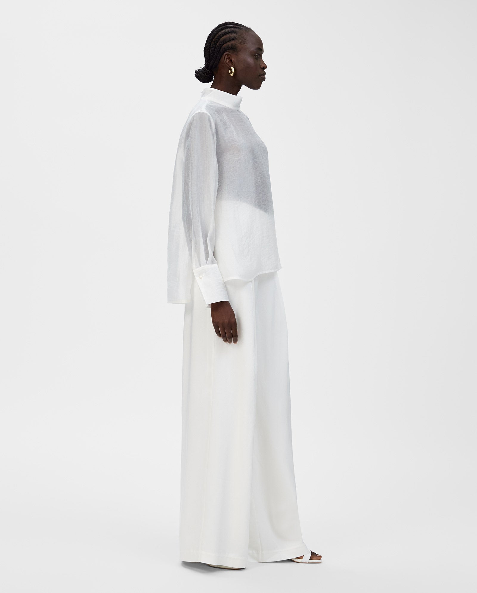A woman in the IVY OAK EBONEY Blouse stands in profile against a plain white background, paired with wide-leg white pants.