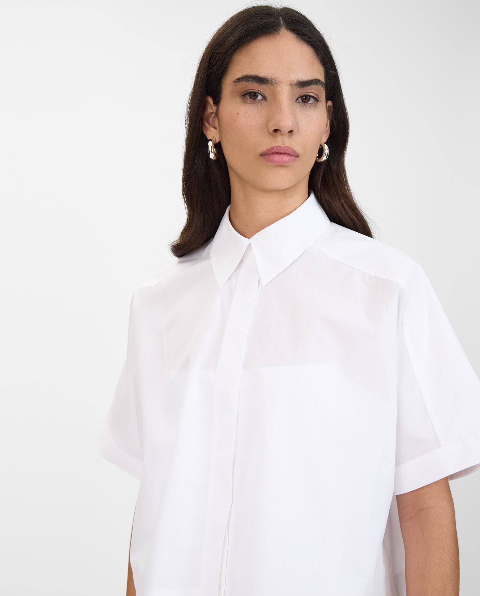 Woman with long dark hair wears the IVY OAK ELVIRA Shirt, a white short-sleeve button-up with detachable sleeves, standing against a plain background.