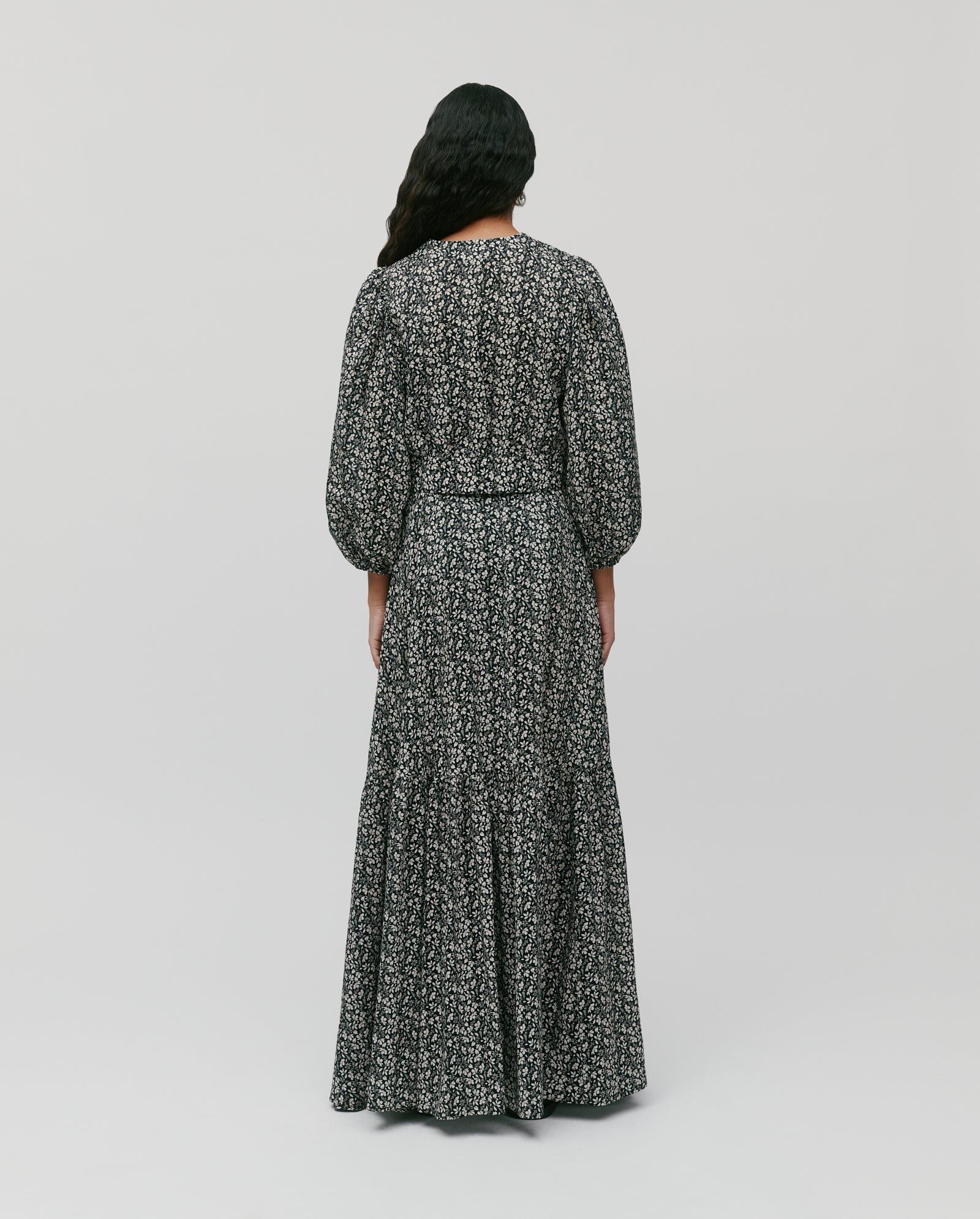 A person with long dark hair, seen from the back, wears the IVY OAK ENRICA Blouse—a black and white floral top with 7/8 balloon sleeves.