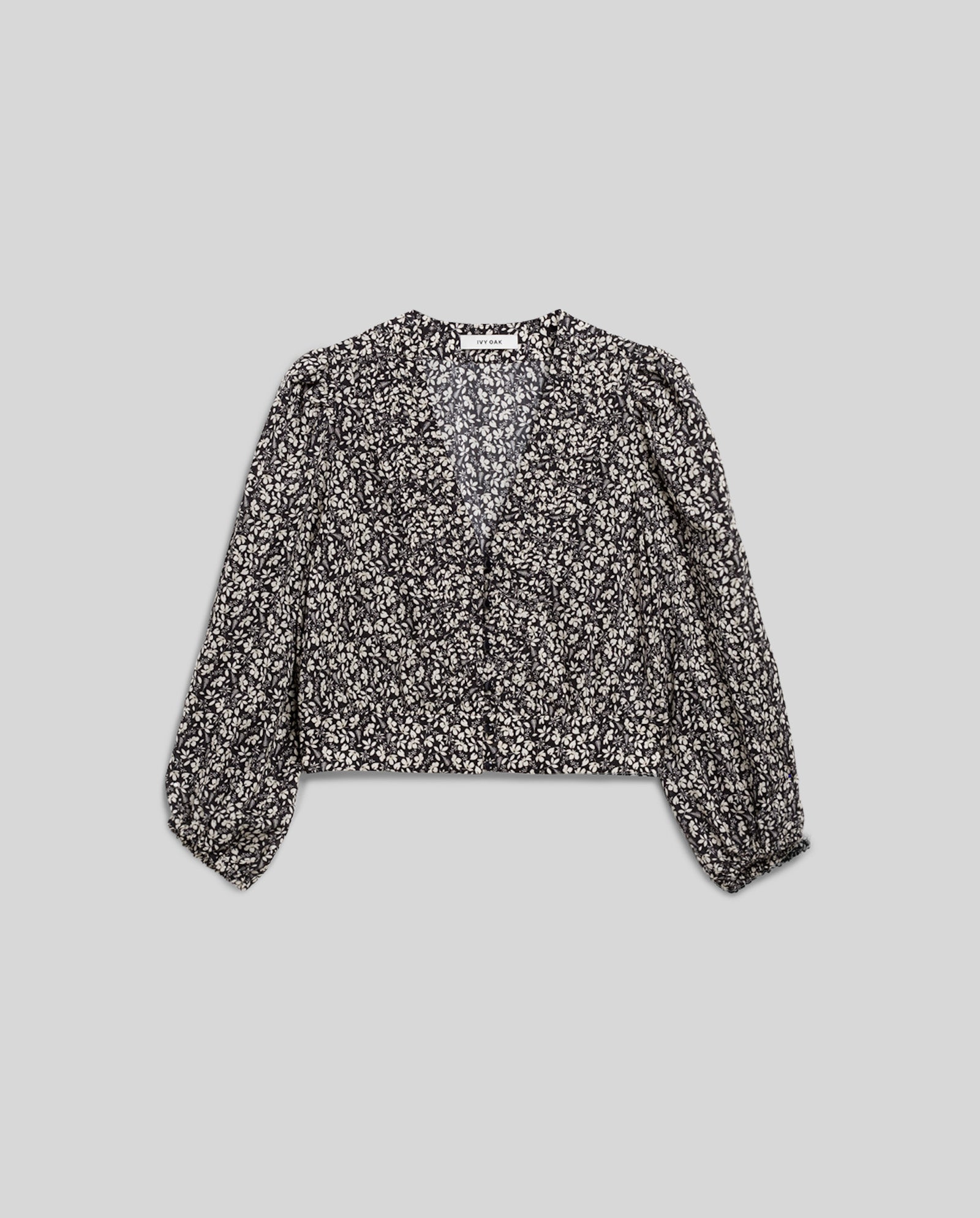 The ENRICA Blouse by IVY OAK is a black, long-sleeved cropped top with a white floral pattern, v-neckline, elasticized cuffs, and 7/8 balloon sleeves for added style.