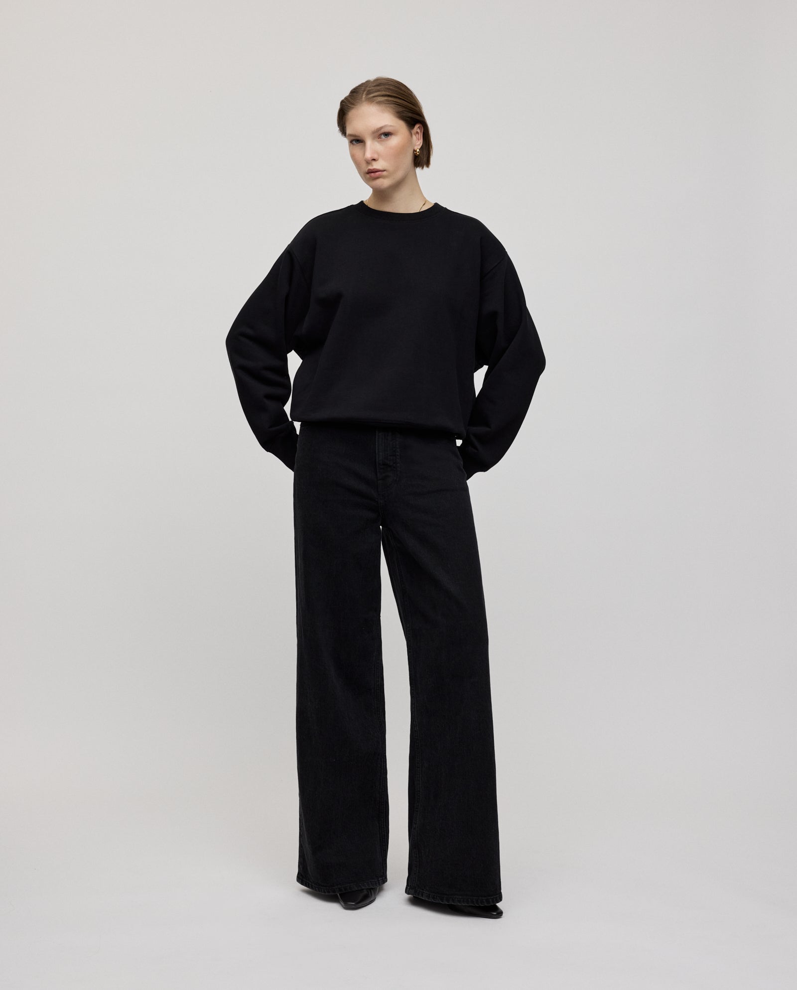 A person wears an oversized IVY OAK KAREN ROSE Jumper with black wide-leg jeans against a plain light background. For a more fitted style, select a smaller size.