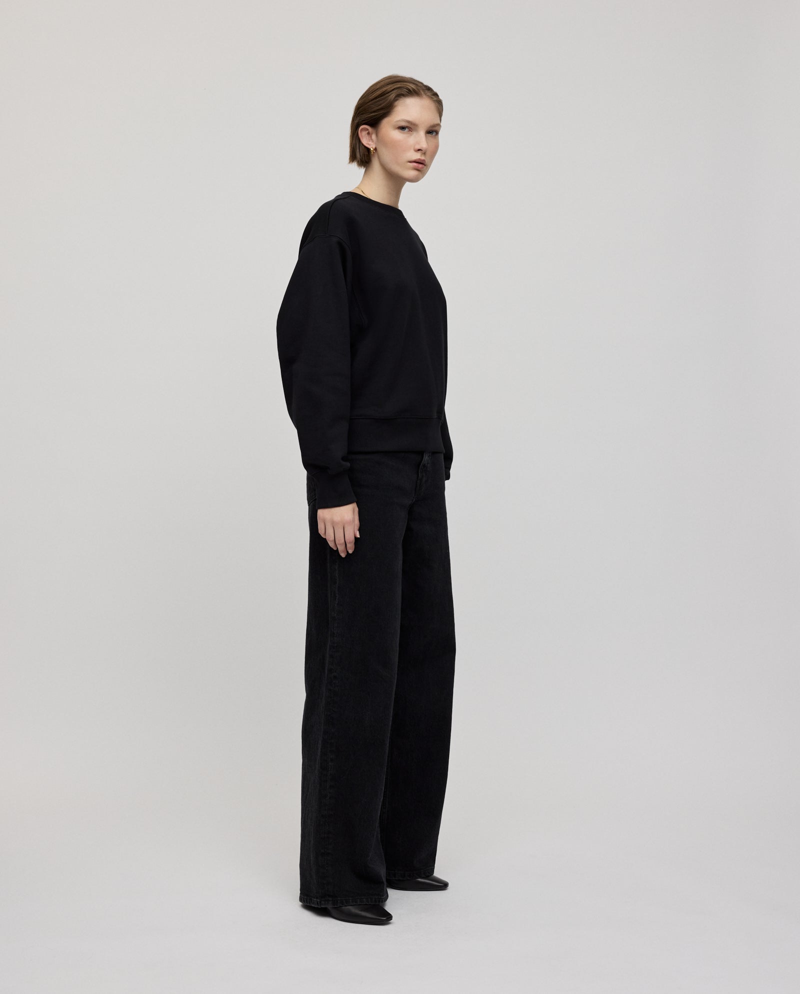 Woman wearing a black KAREN ROSE Jumper by IVY OAK with an oversized fit and wide-leg black pants against a plain background—consider sizing down for a closer fit.