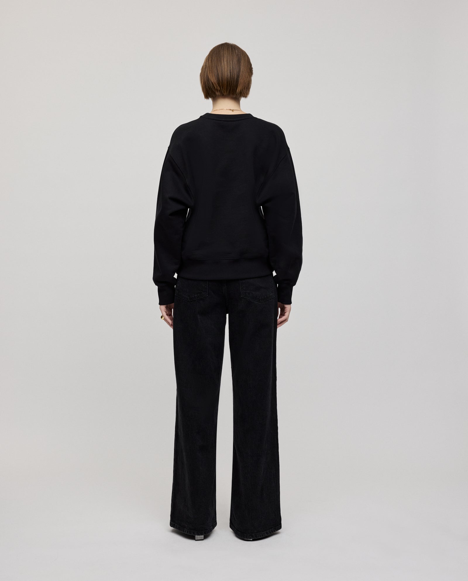 Person facing away, wearing an oversized black IVY OAK KAREN ROSE Jumper and wide-leg black pants against a plain background; for a closer fit, select a smaller size.