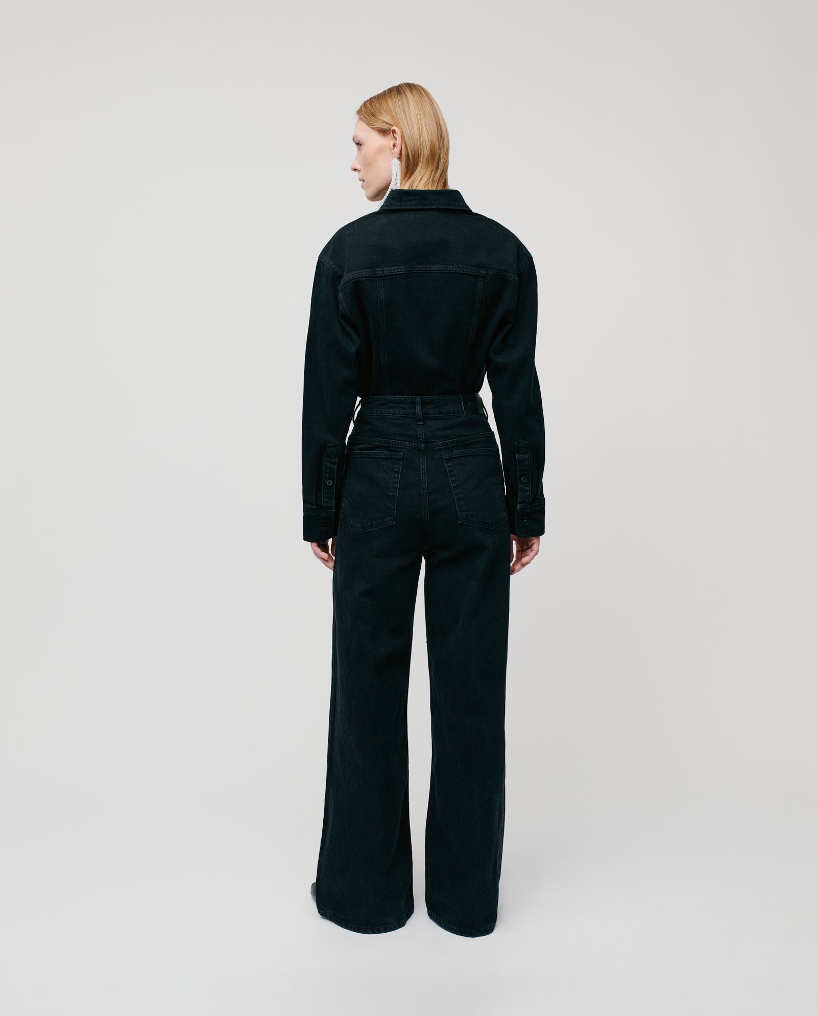 A person with blonde hair, standing and facing away from the camera, is wearing the BERENICE Blouse by IVY OAK.